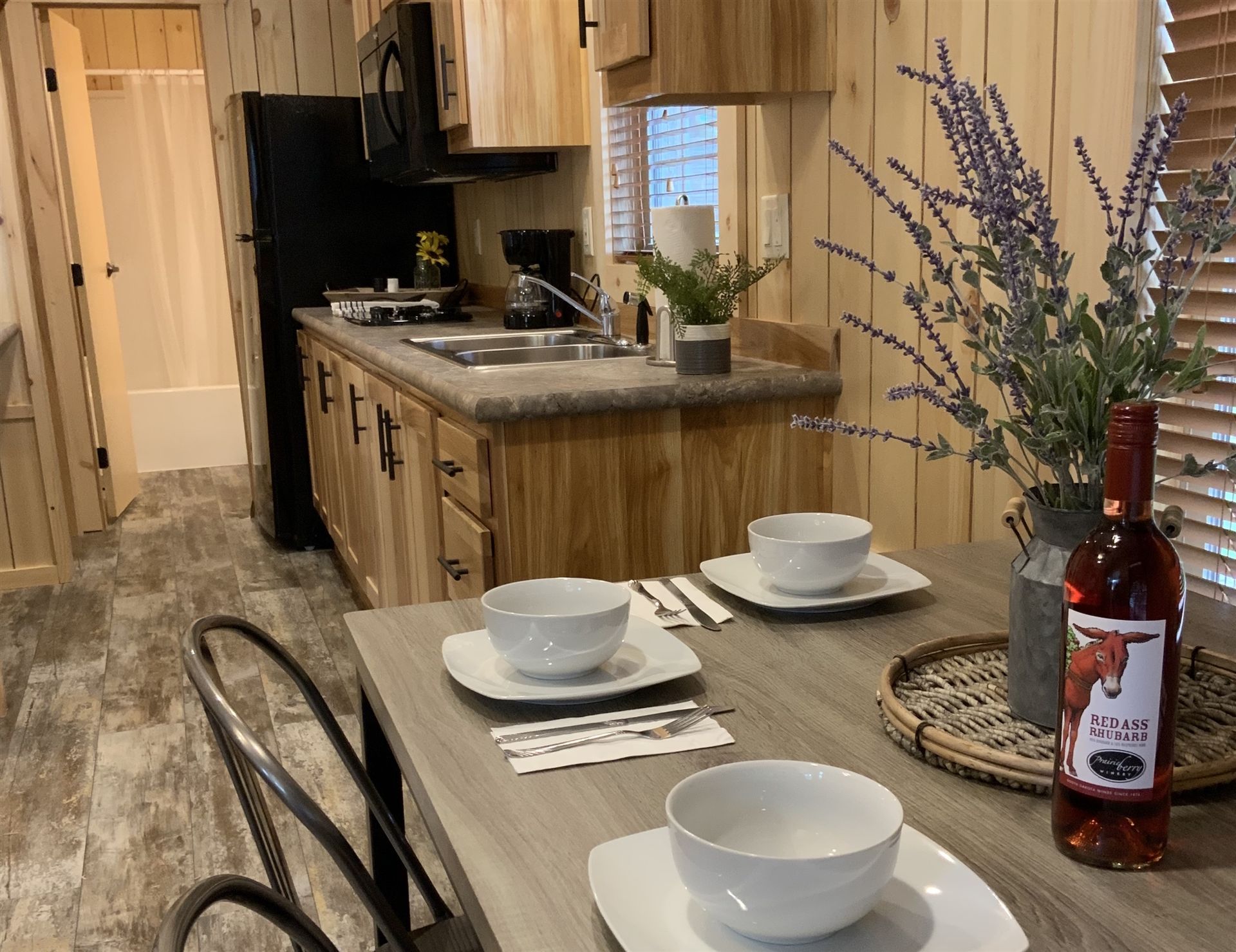 Cozy cabin kitchen with dining table set for two.  Includes fridge, stove, sink, and decorative flowers/wine.