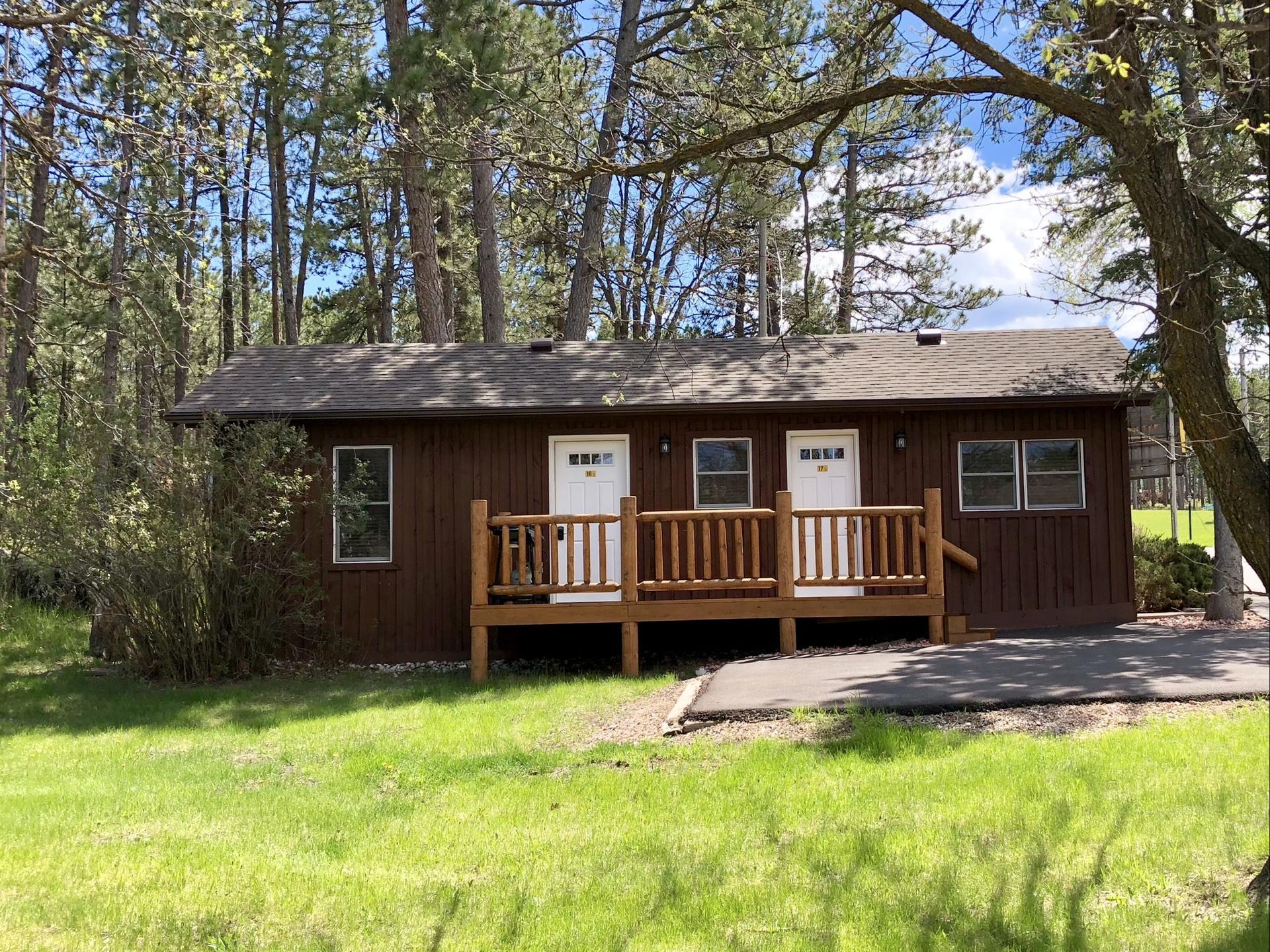 Brown cabin with white doors, porch, and windows, set in a grassy area with trees.