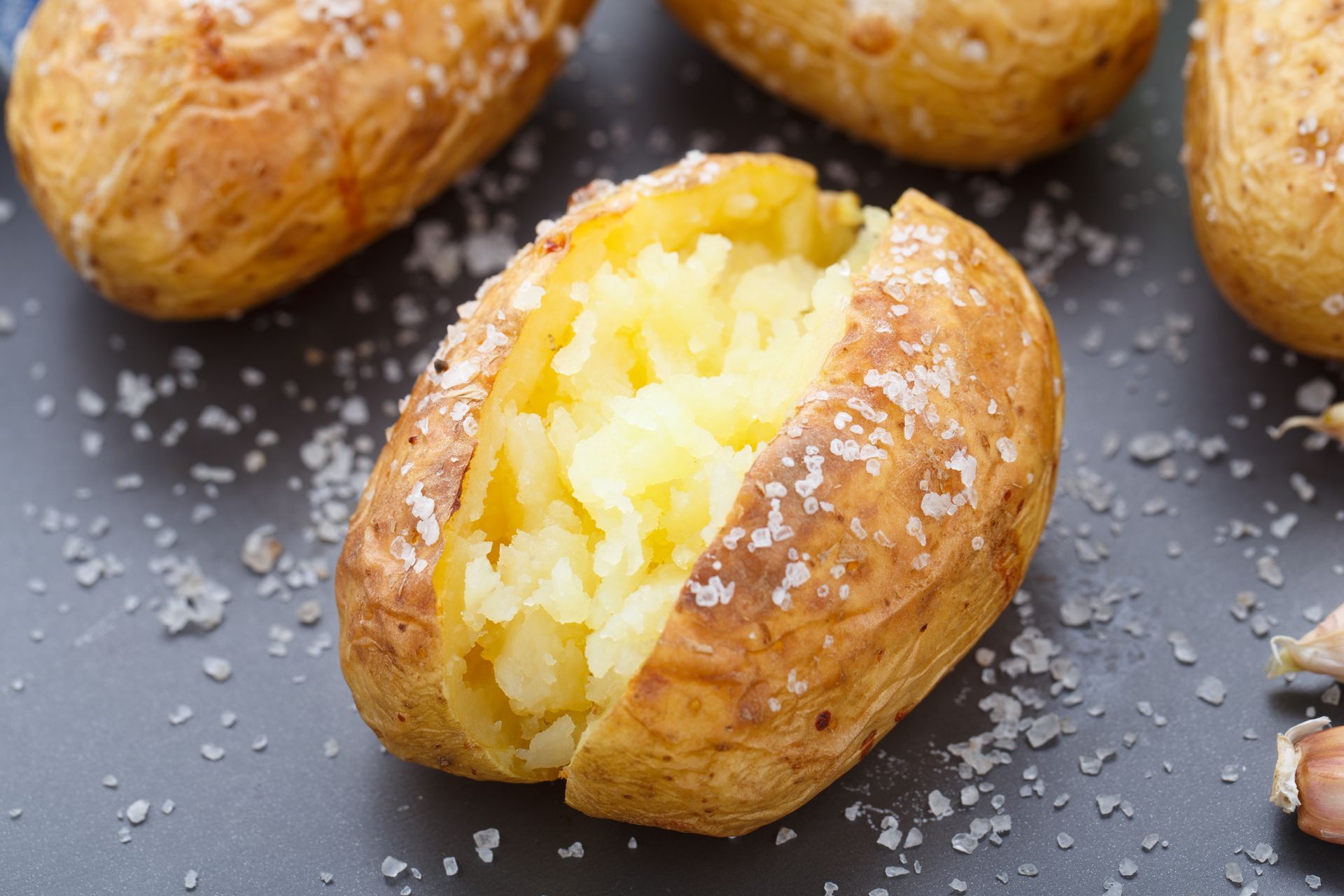 Baked potato, split open, with fluffy interior and sprinkled salt on gray surface.