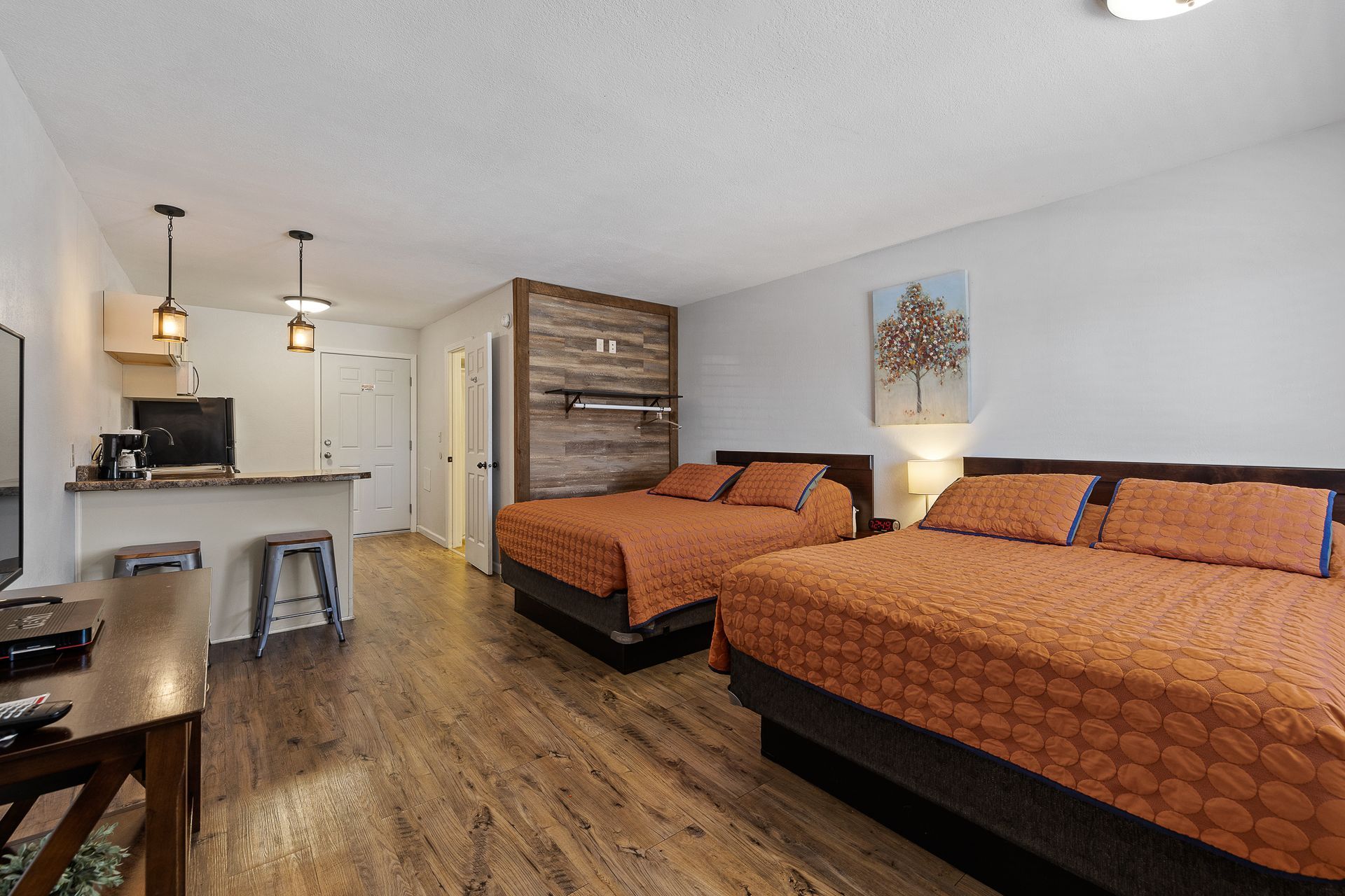 Studio apartment with two orange-covered beds, a kitchen bar, and wooden floors.