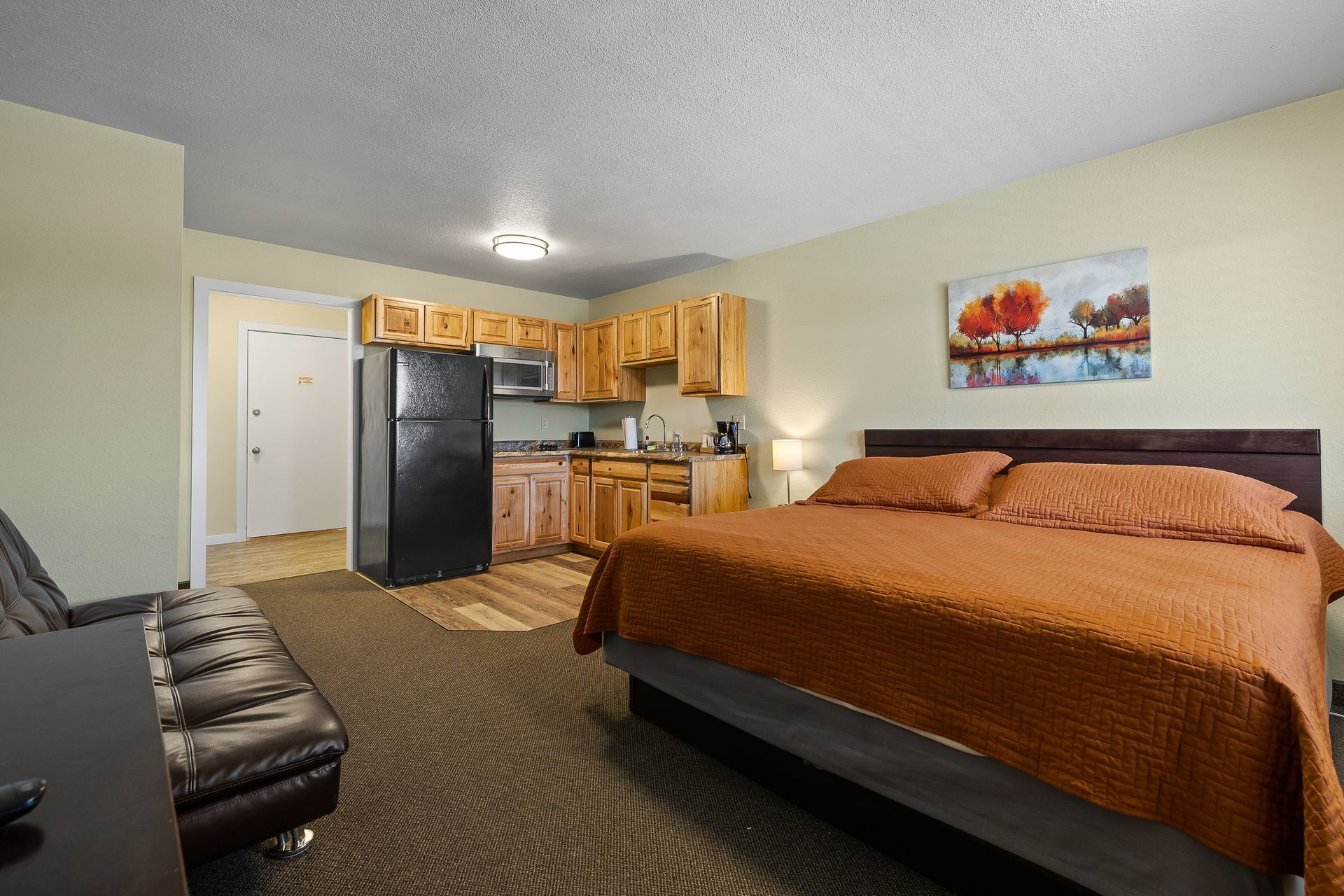 Studio apartment with kitchen, bed, and sofa. Brown and orange color scheme.