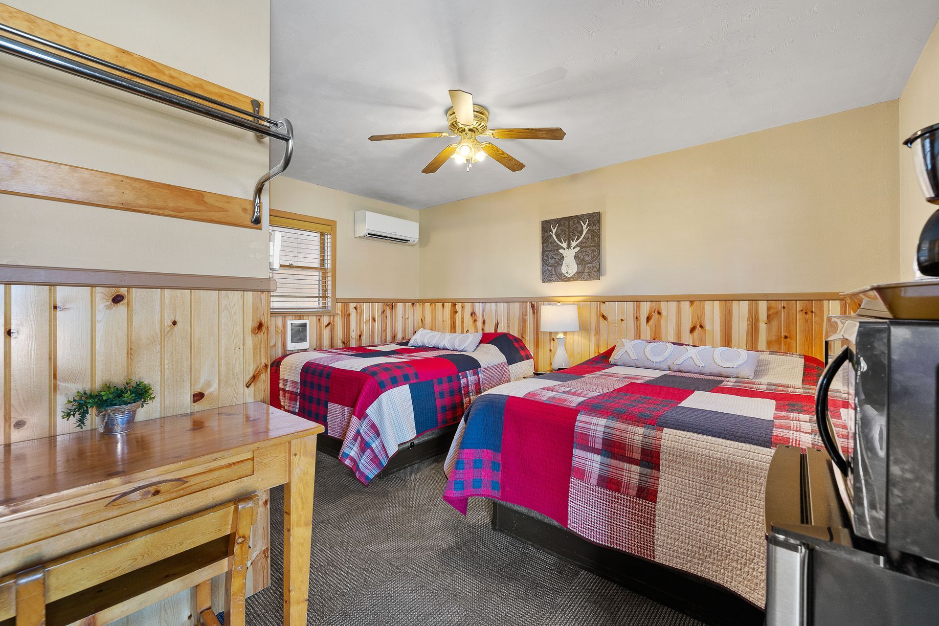 A motel room with two beds, quilt bedspreads, wood paneling, and a small table.