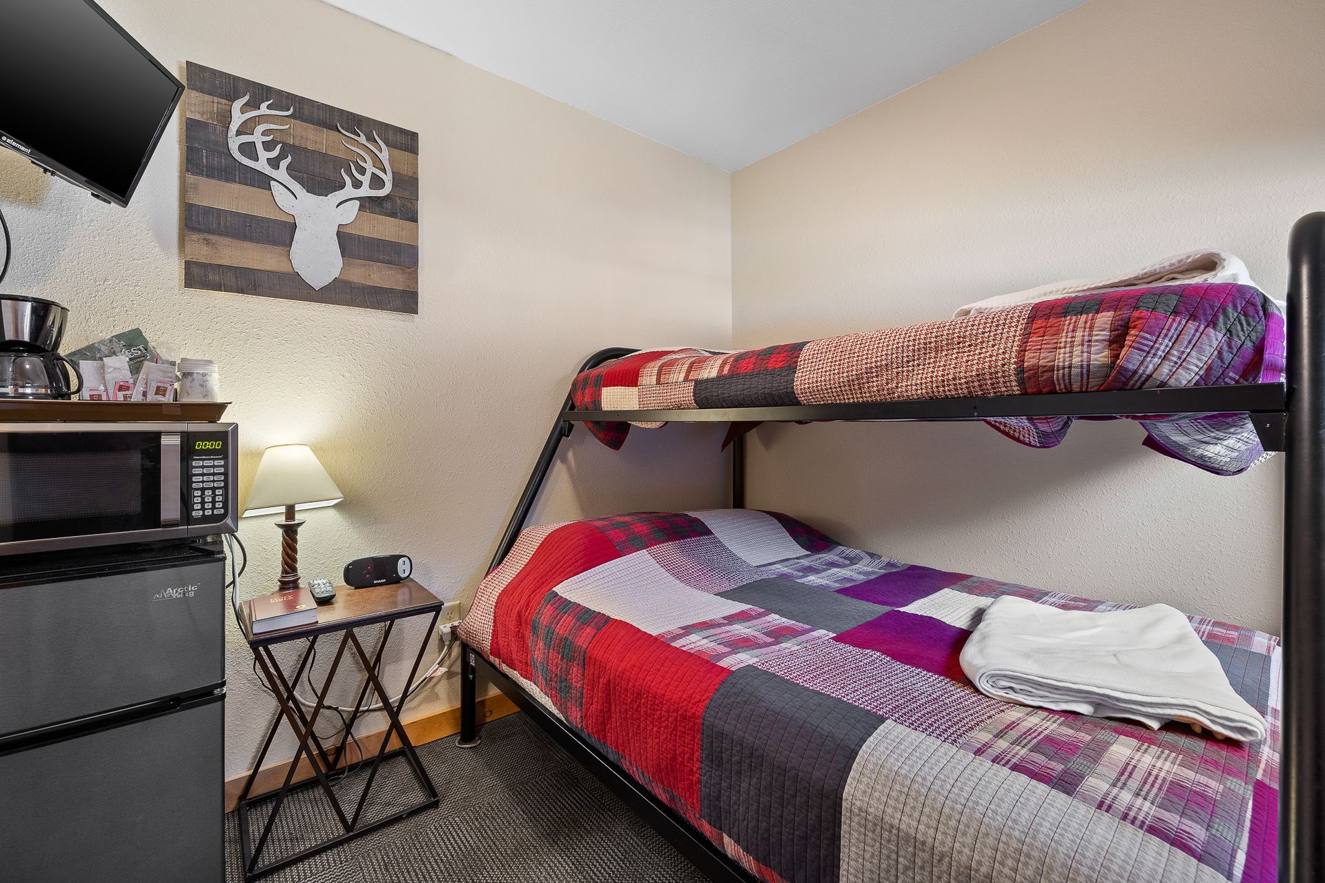 Small bedroom with bunk beds, microwave, and small table. Walls are beige, with decorative deer head.