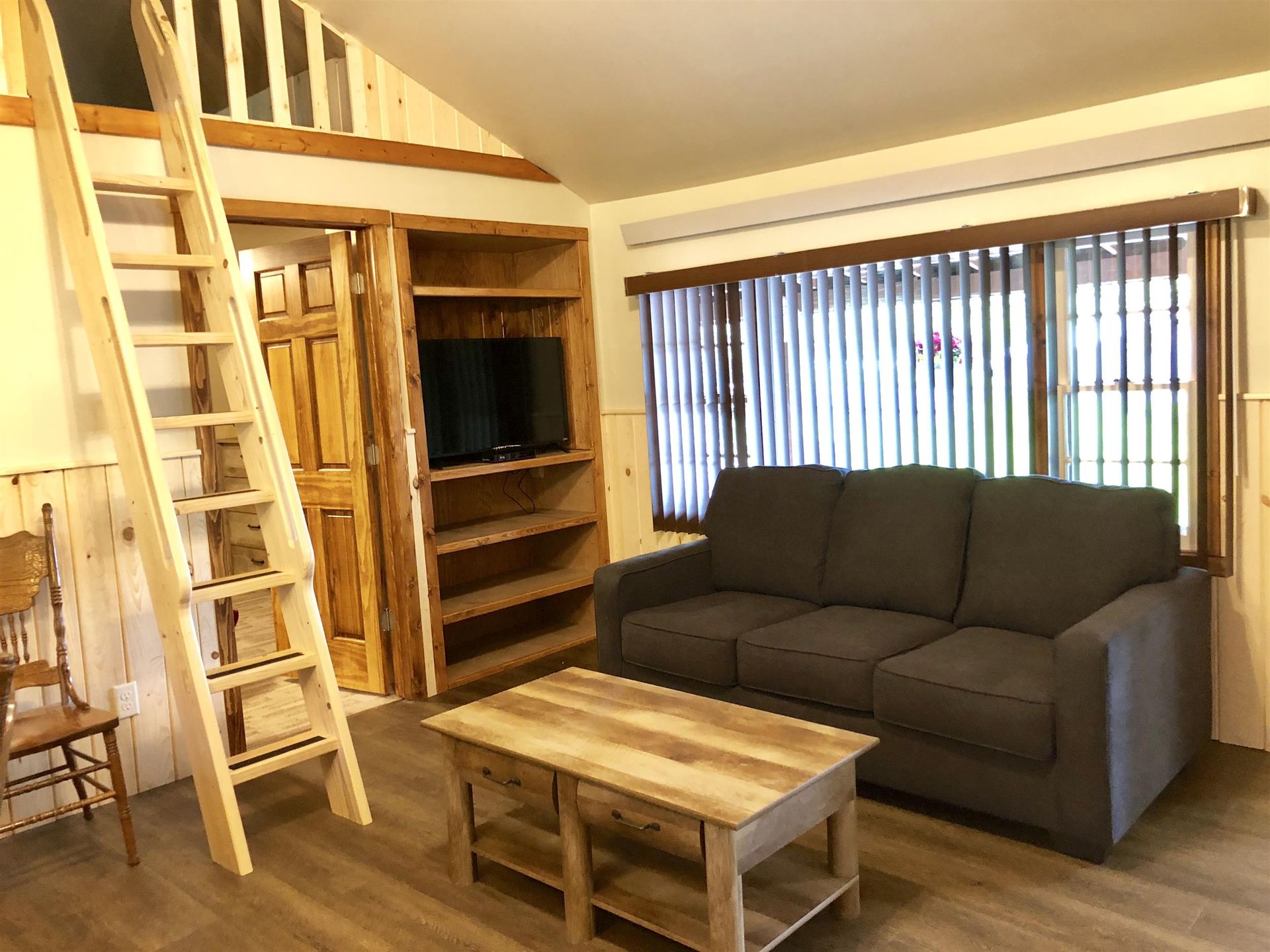 Cozy living room with a couch, coffee table, built-in shelves with TV, and a ladder to a loft.