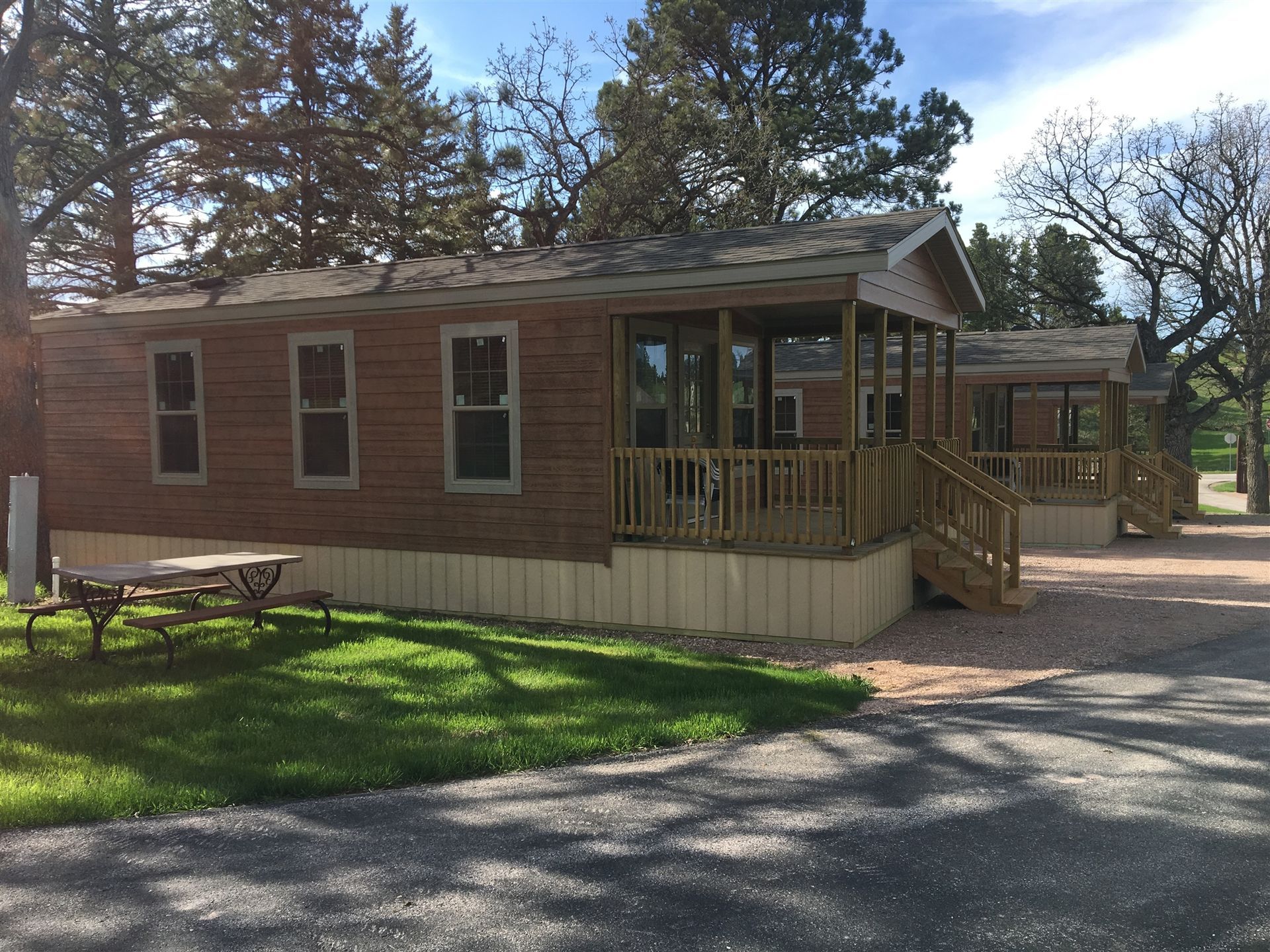 Wooden cabins with screened-in porches, parked next to green grass and a gravel driveway.
