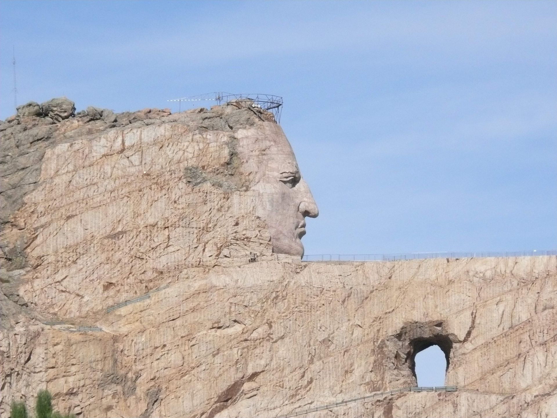 Rock formation carved like a human face with a small arched opening beneath, against a blue sky