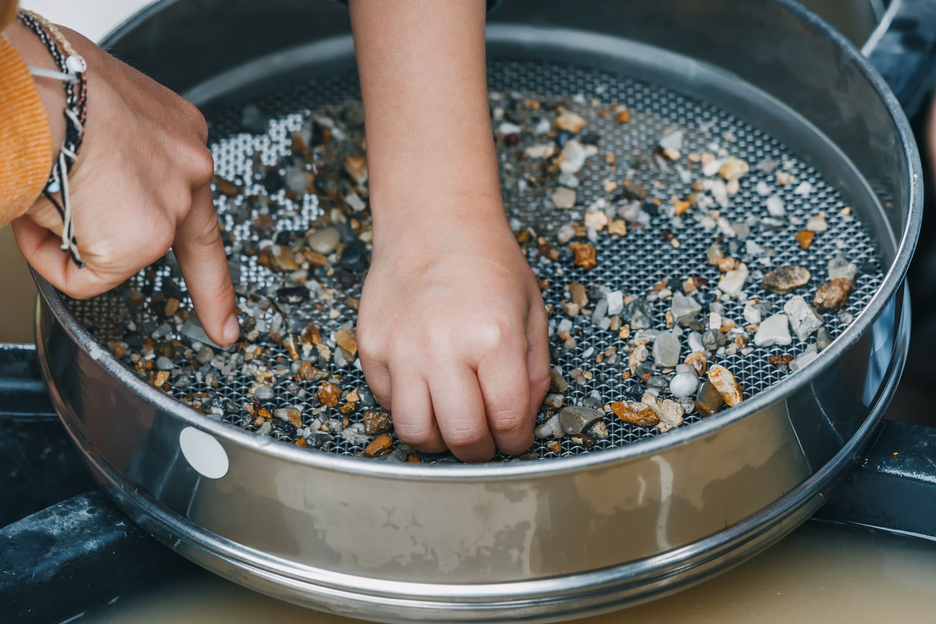 Hands sifting mixed pebbles in a metal tray sieve