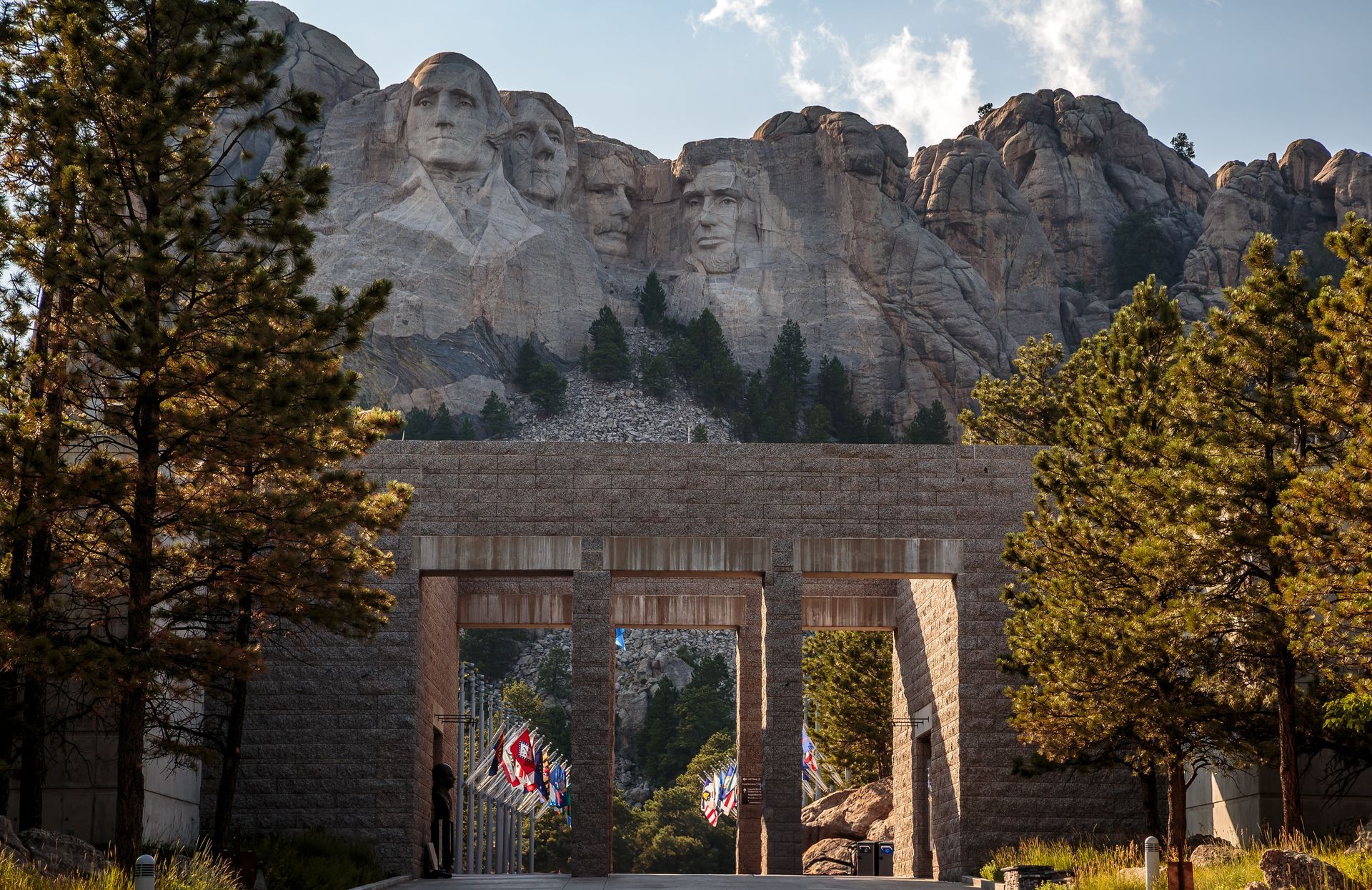 Stone archway entrance with people, trees, and a mountain cliff in the background