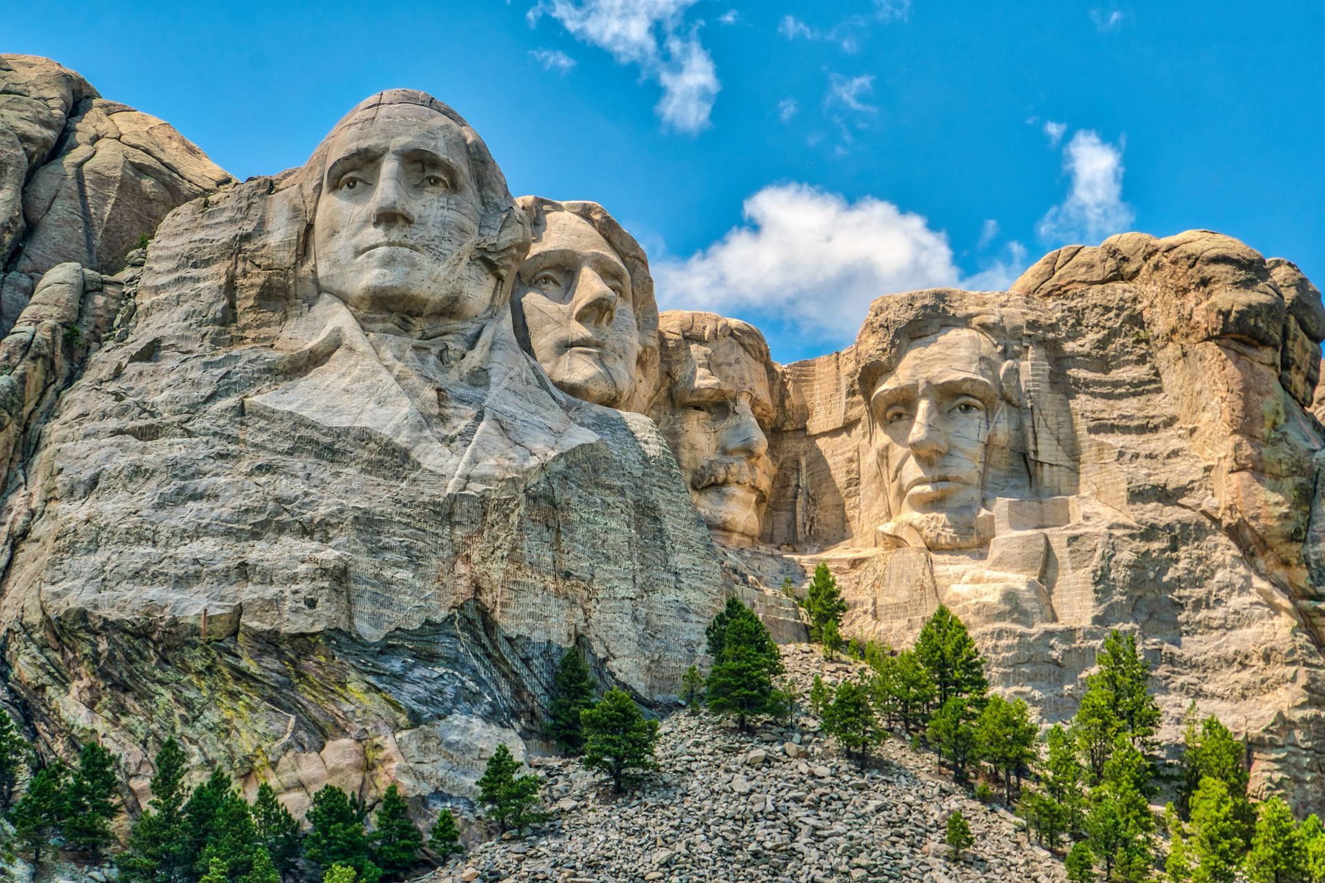 Mount Rushmore carved into a granite mountain under a blue sky with clouds