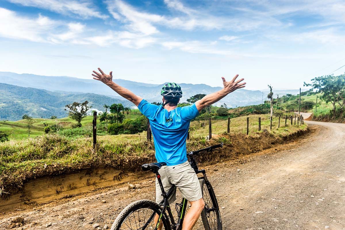 A man is riding a bike down a dirt road with his arms outstretched.