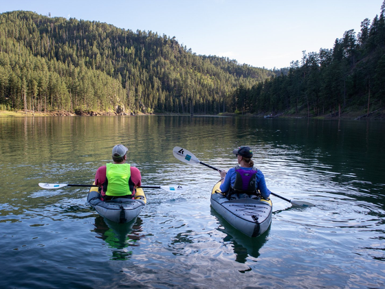 Two people are paddling kayaks on a lake.