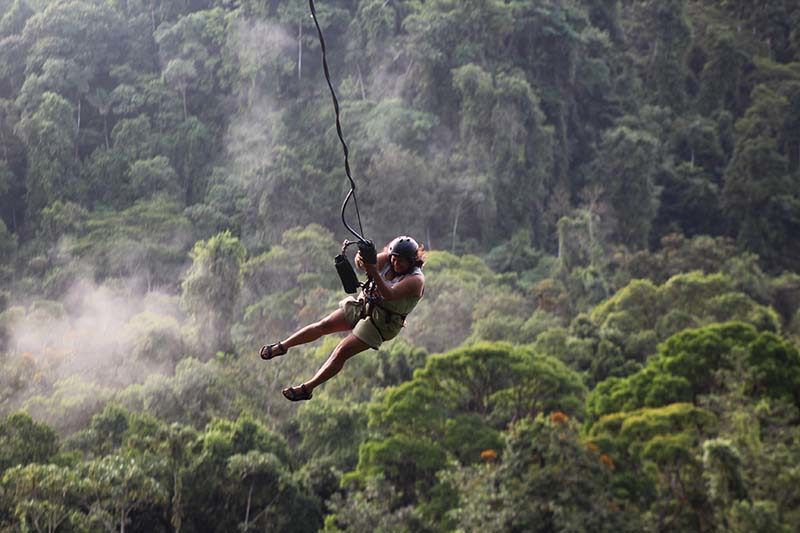 A person is flying through the air on a zip line in the jungle.
