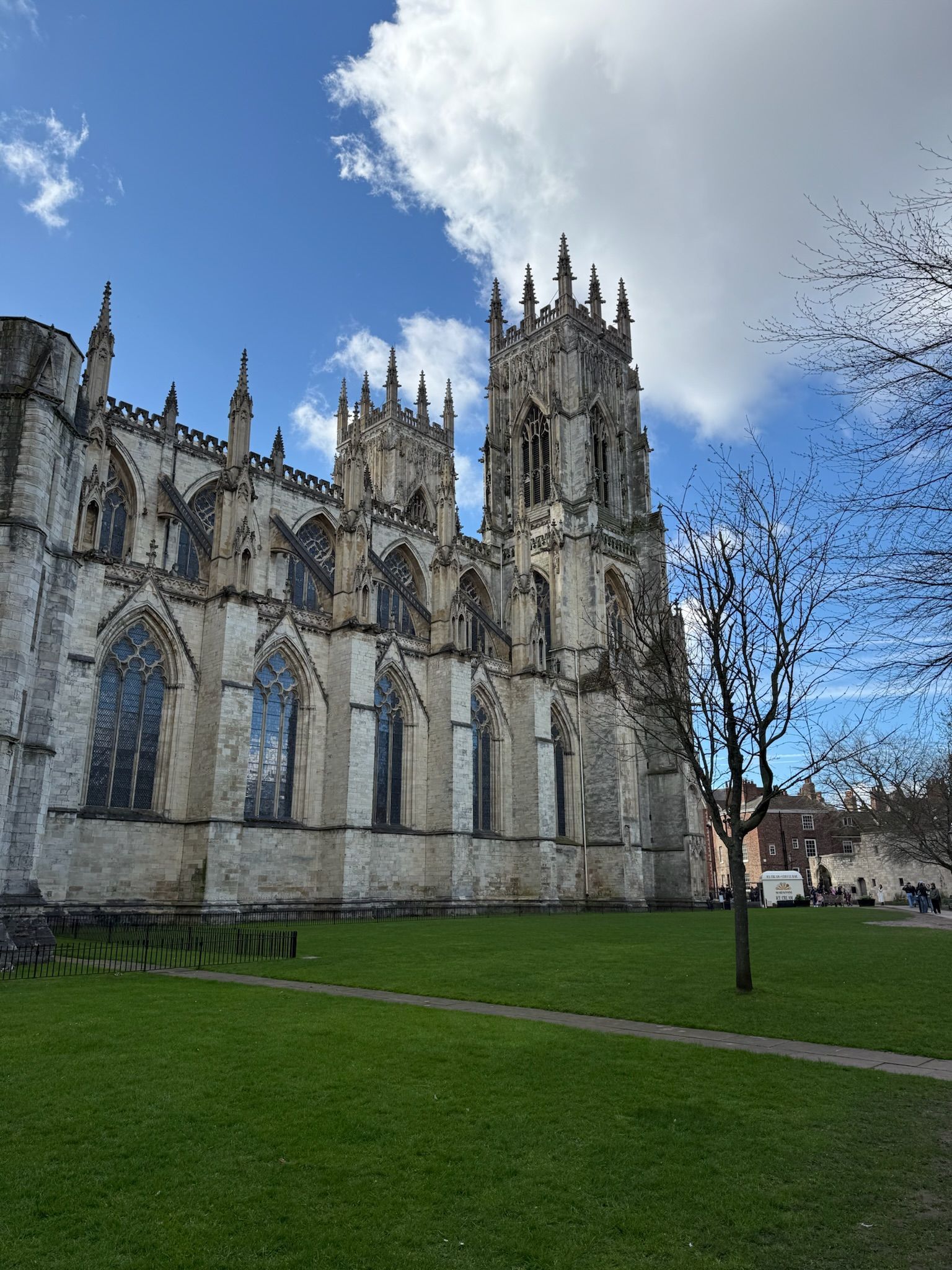 Gothic stone cathedral with tall tower beside a green lawn under a partly cloudy blue sky