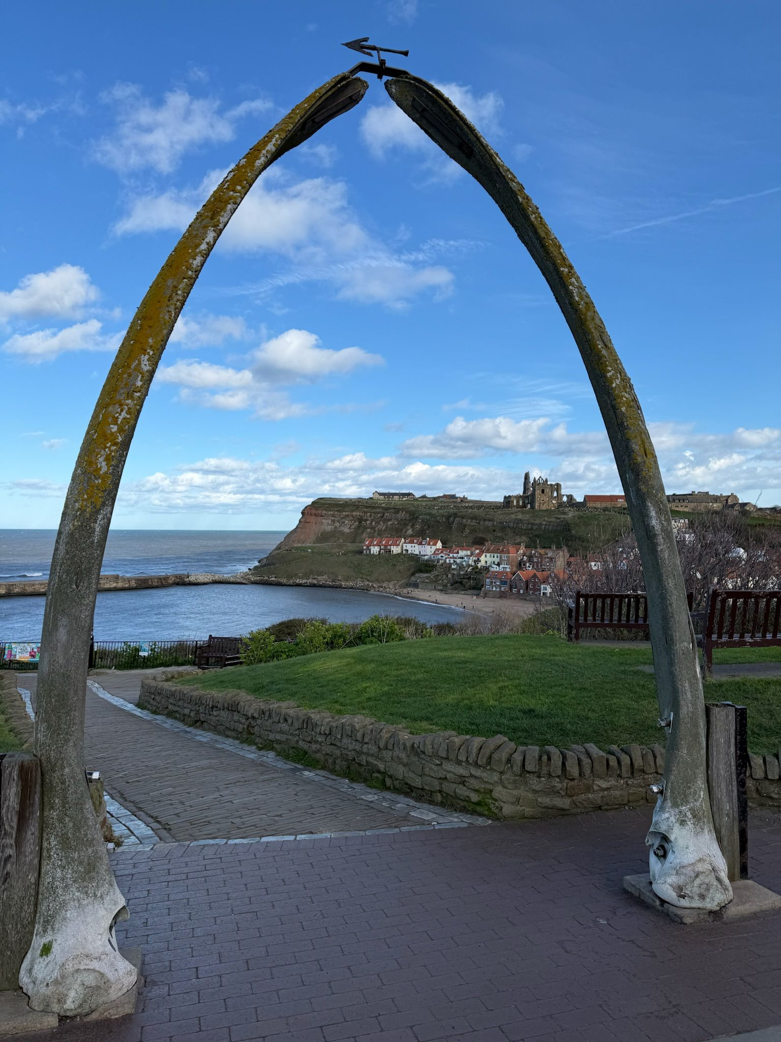 Whale jawbone arch framing a coastal harbor and cliffside town under a blue sky