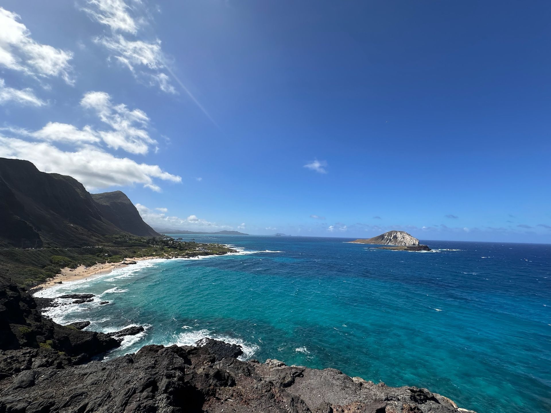 Coastal bay with turquoise water, rugged cliffs, white surf, and a bright blue sky