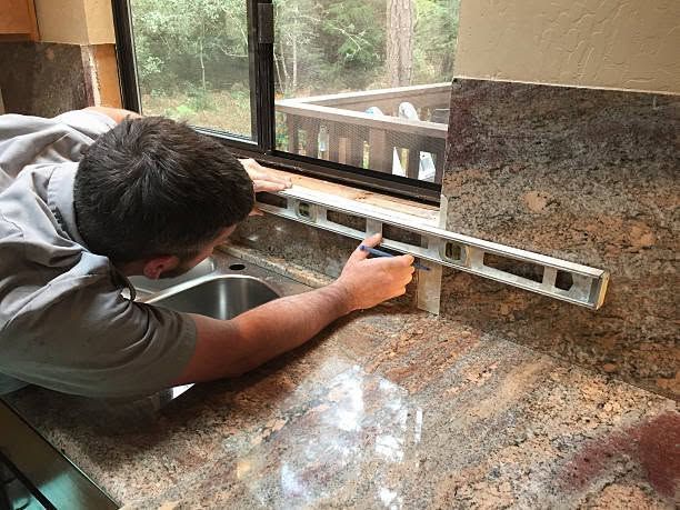 Person measuring a granite countertop backsplash with a spirit level in a kitchen.