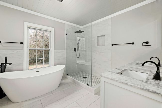 Bright white bathroom with freestanding tub, glass shower, marble vanity, and window light