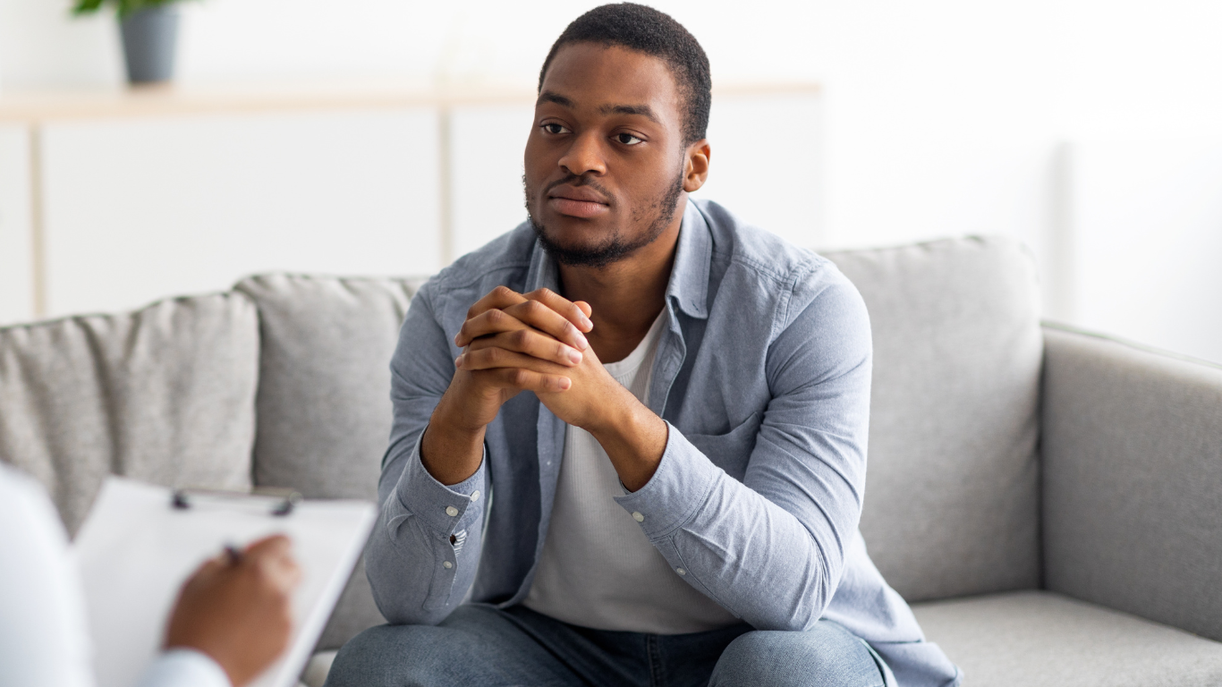Therapist taking notes on a clipboard while a couple sits blurred in the background on a sofa