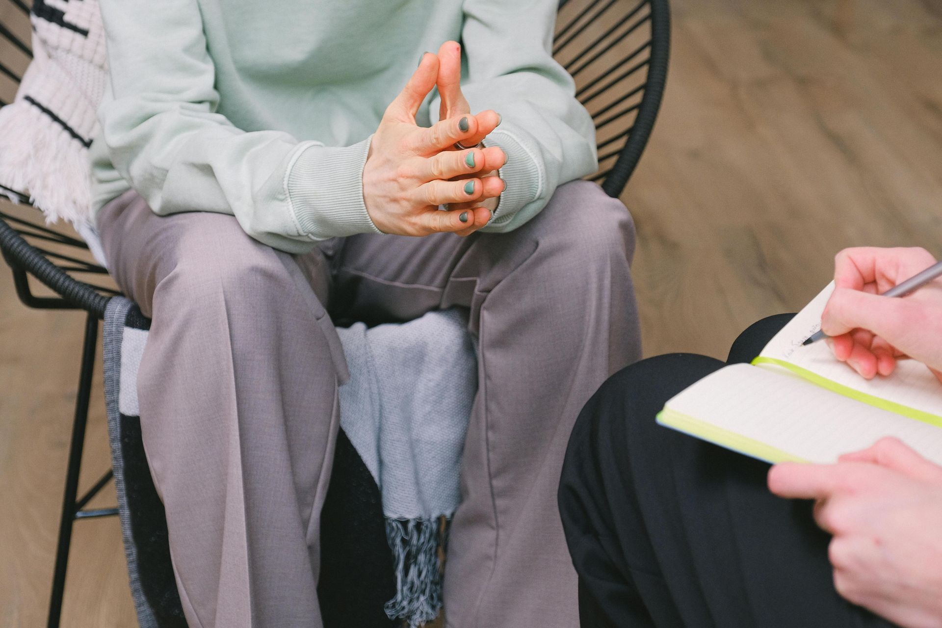 Two people seated in a counseling session, one gesturing and one taking notes on a notepad