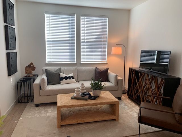 A modern living room with a beige sofa, wooden coffee table, floor lamp, and a brown leather chair on a neutral area rug.