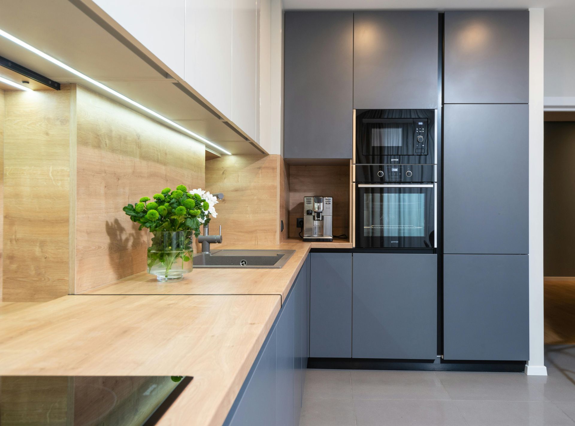 A kitchen with gray cabinets , wooden counter tops , a sink , and a microwave.