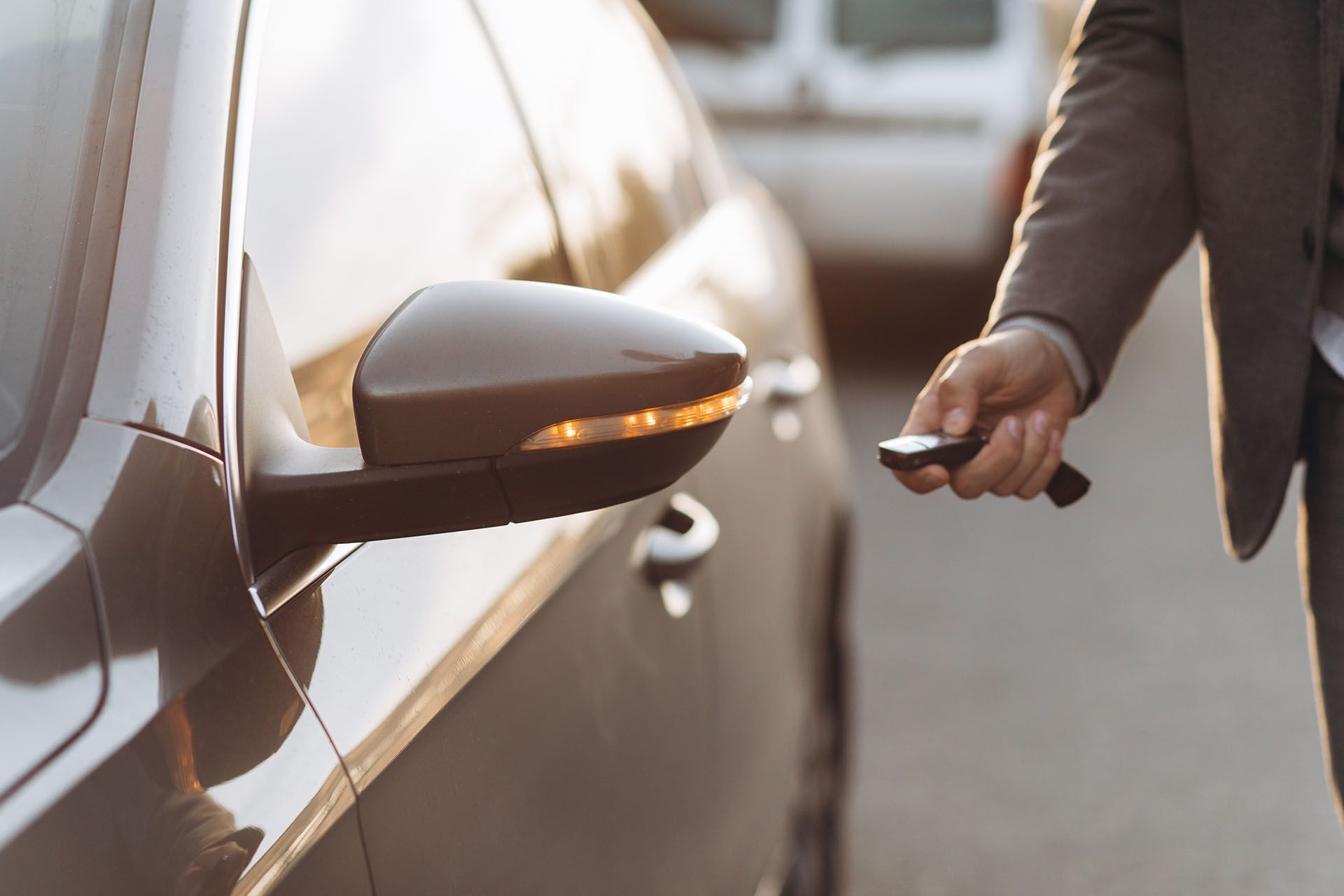 Car owner holding a key fob beside a parked car, with the side mirror and door visible.