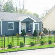 Small blue house with black fence, front porch, and a hanging chair in the yard