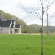Suburban house with a large green lawn and young trees under a cloudy sky