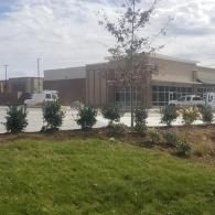 Modern brick building with large windows, trees, and a grassy foreground under a cloudy sky