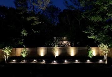 Illuminated stone wall and trees at night with landscape spotlights and dark sky