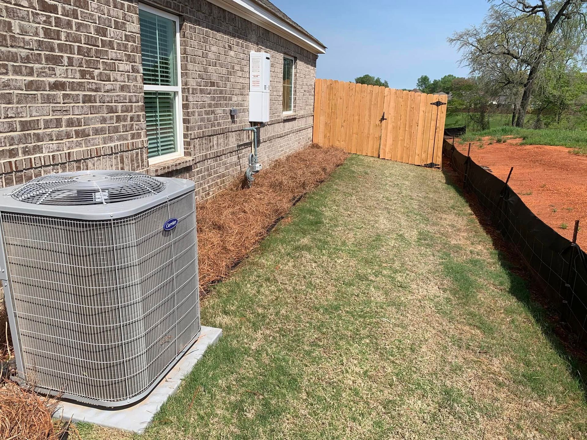 A brick house with a wooden fence and a gray air conditioner in the backyard.