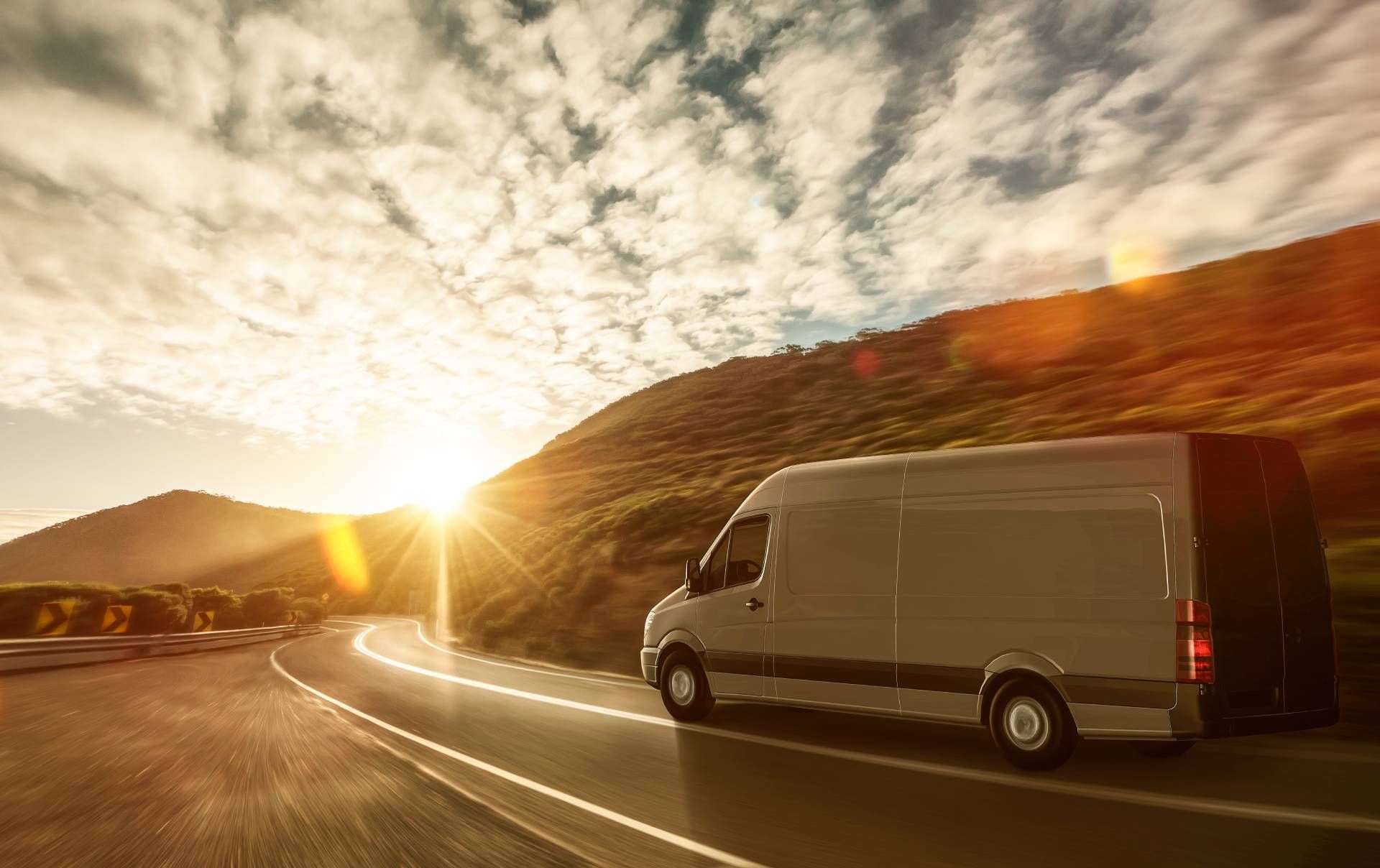 White cargo van driving on a winding road at sunset beside rocky hills