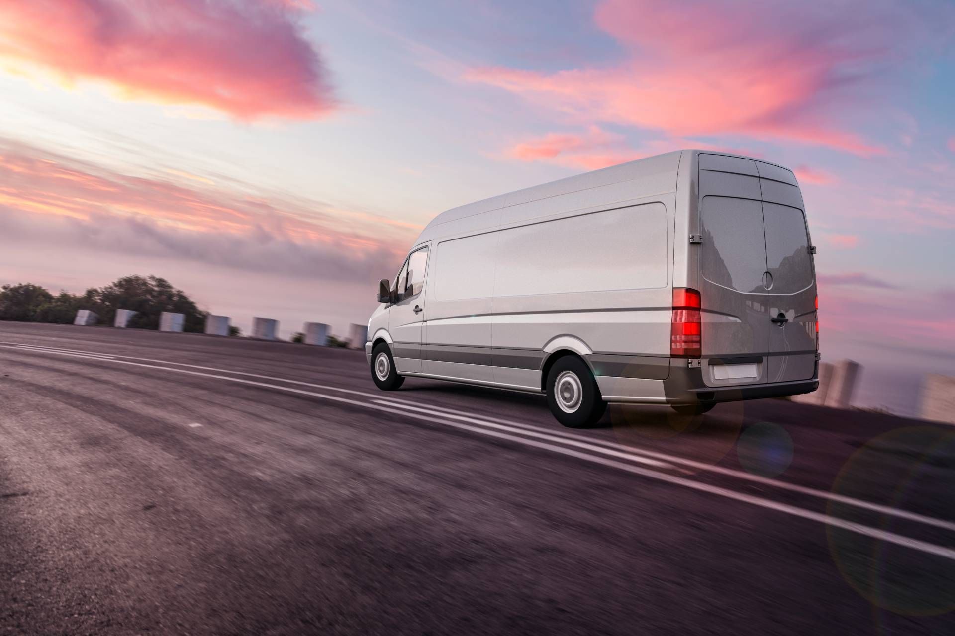 Silver cargo van driving on a highway at sunset, with motion blur and pink clouds overhead
