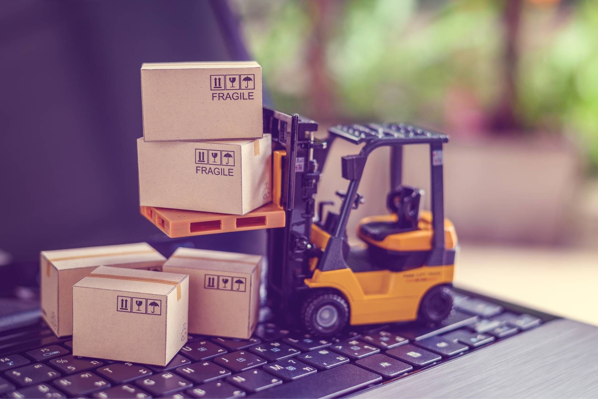 Small yellow forklift stacking cardboard boxes on a laptop keyboard