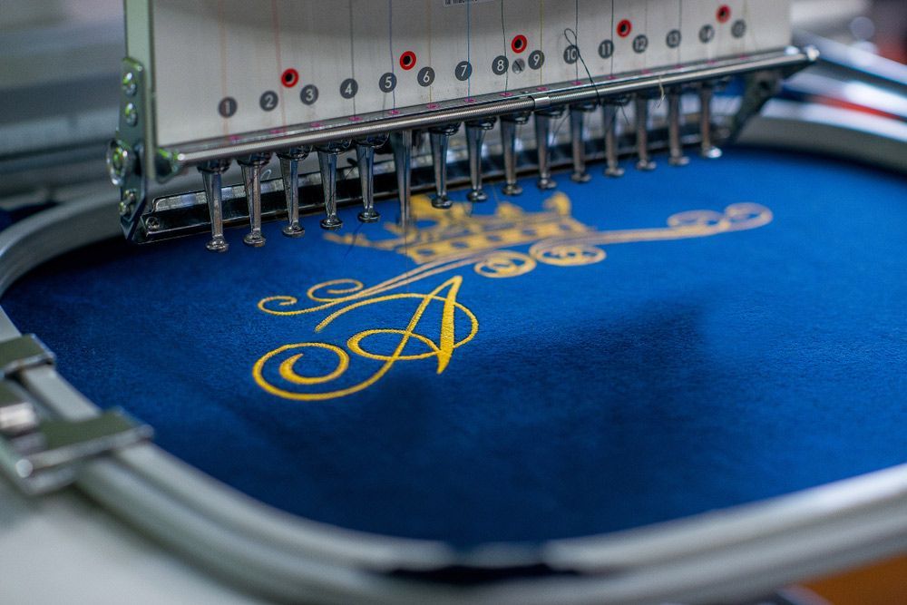 A Machine is Embroidering a Letter  On a Blue Cloth — Embroidery Express in Nambour, QLD