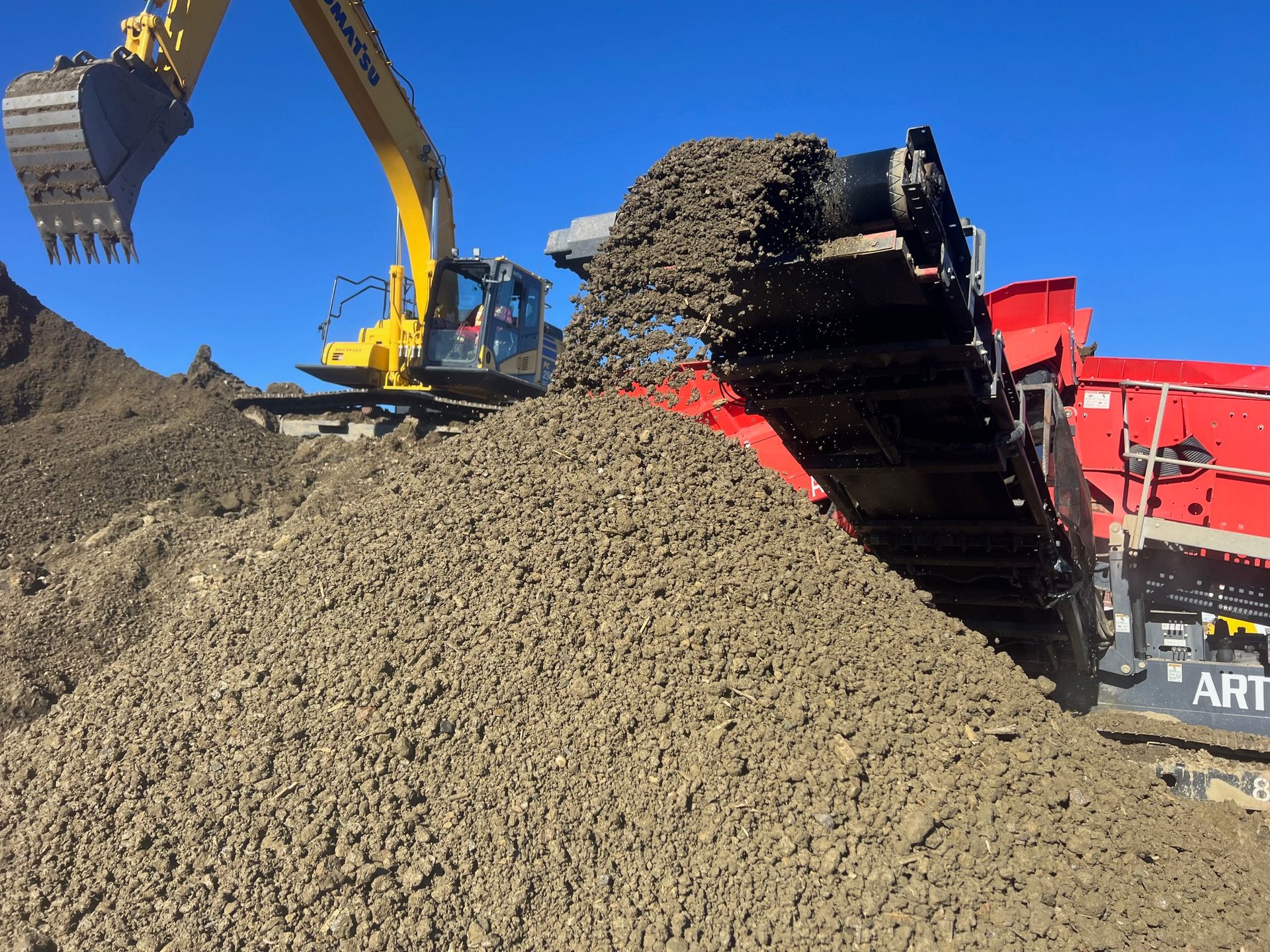 A yellow excavator is digging into a pile of dirt