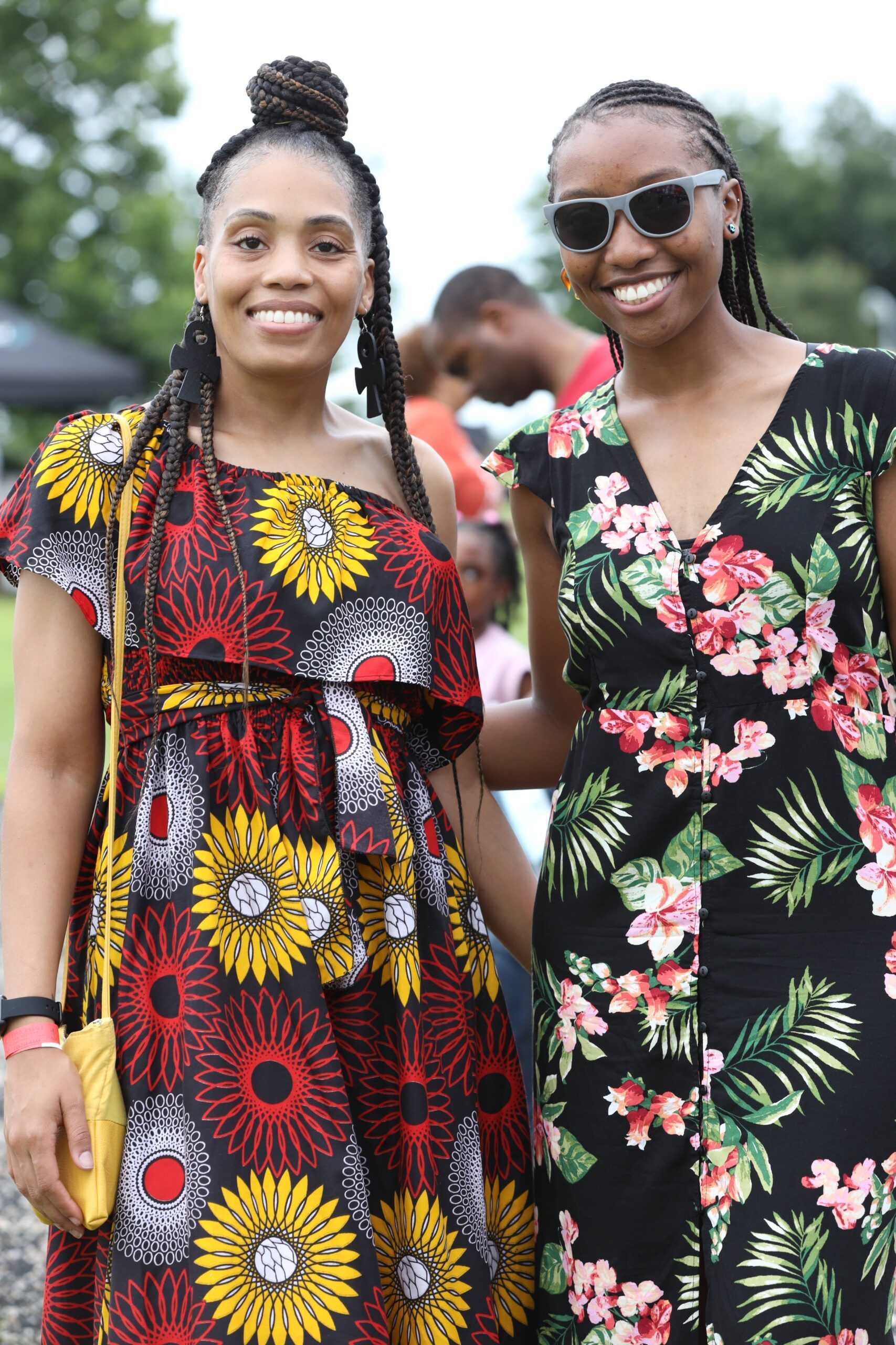 Two smiling people in colorful floral dresses standing outdoors at an event