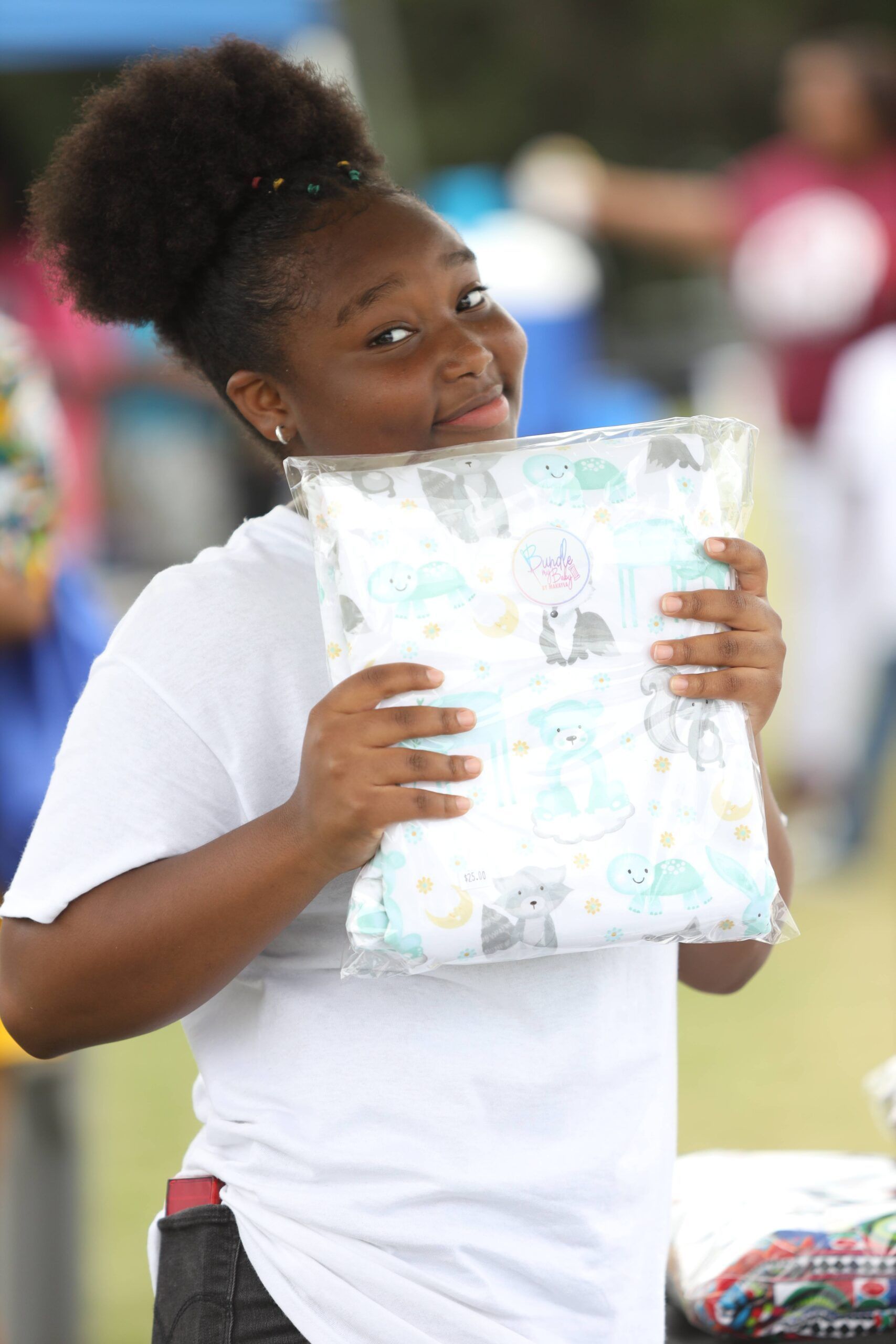 Person in a white shirt smiling and holding a wrapped gift outdoors.
