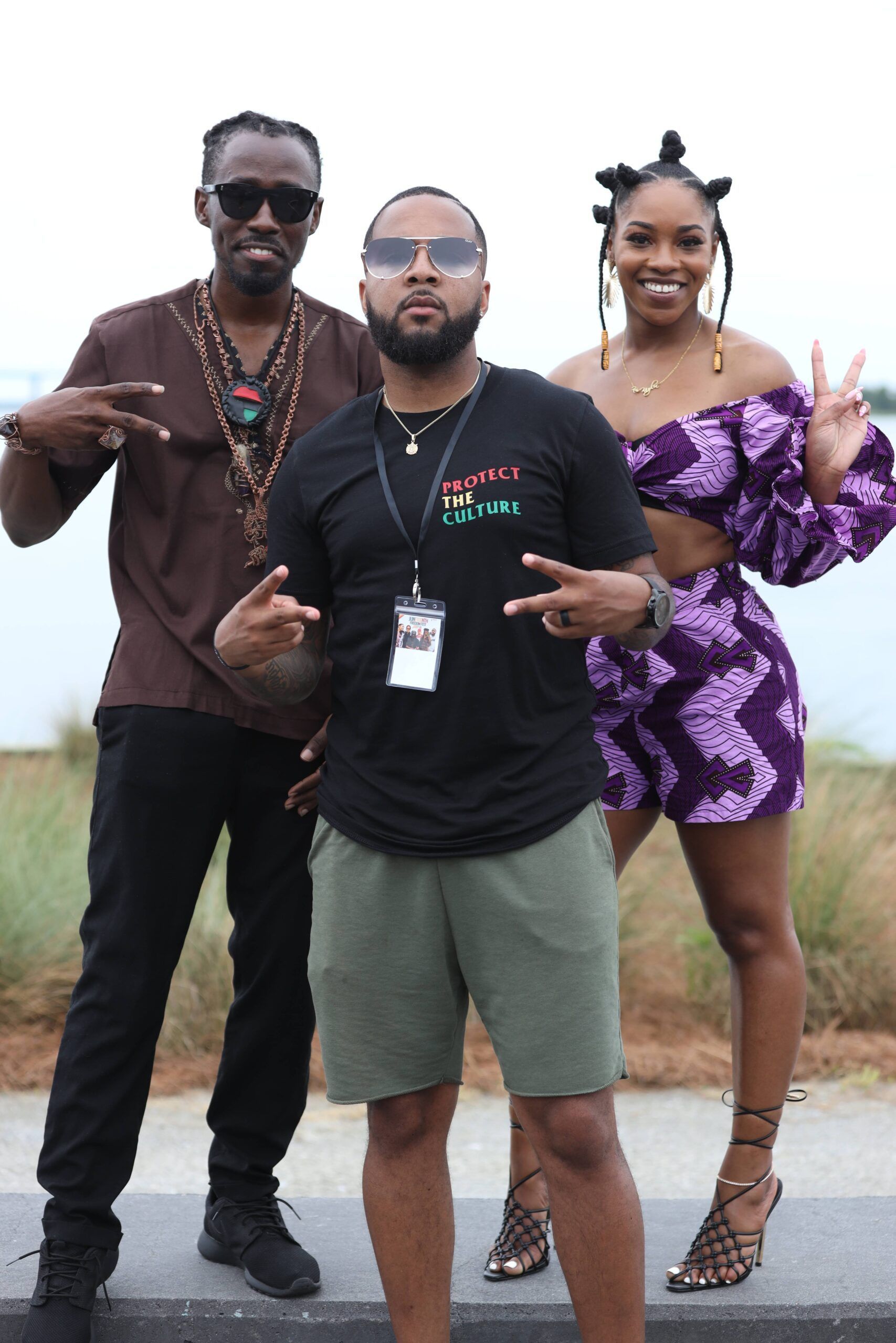 Three people posing outdoors, two flashing peace signs, one in a black shirt and green shorts