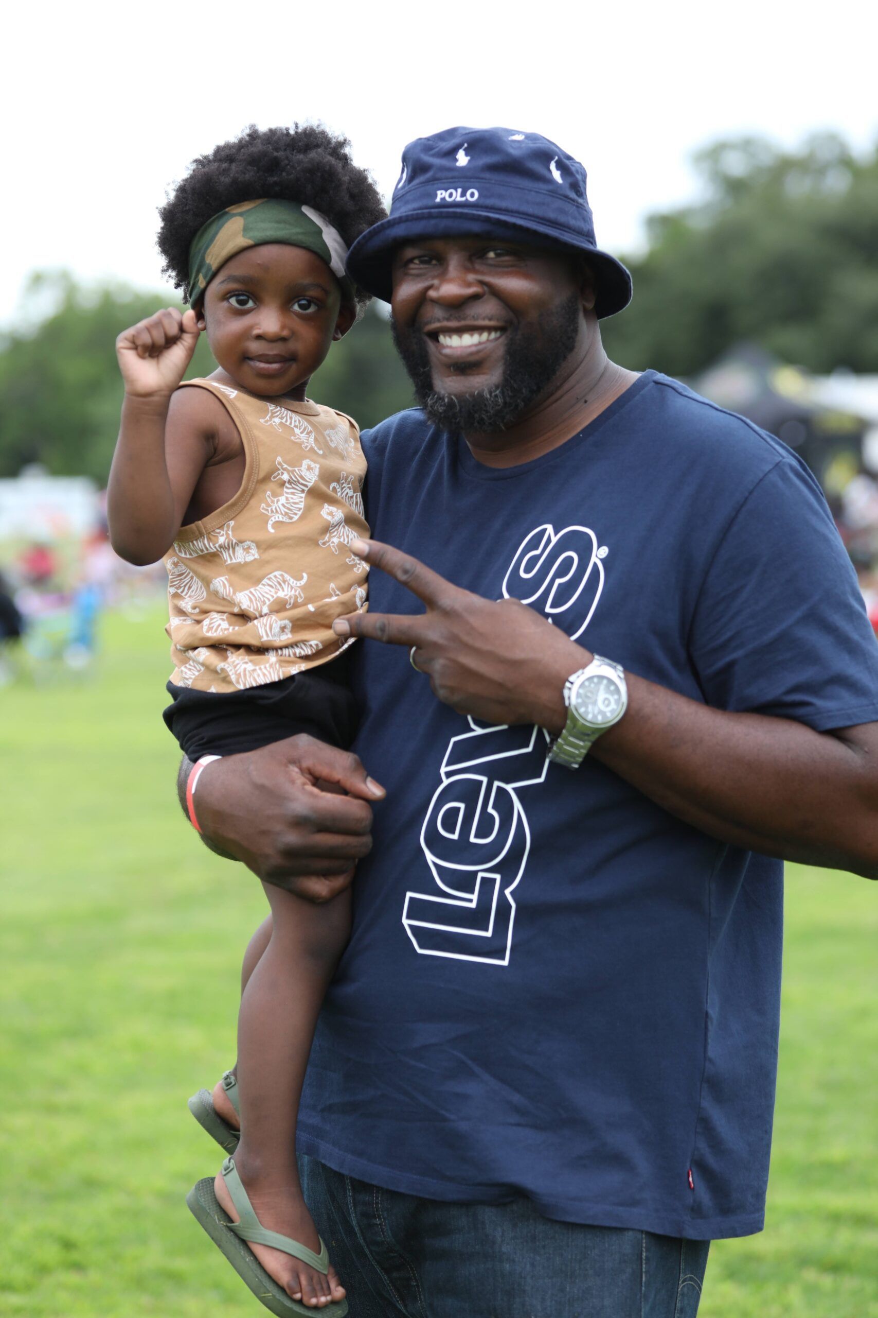 Man in blue shirt and bucket hat holding a smiling child outdoors