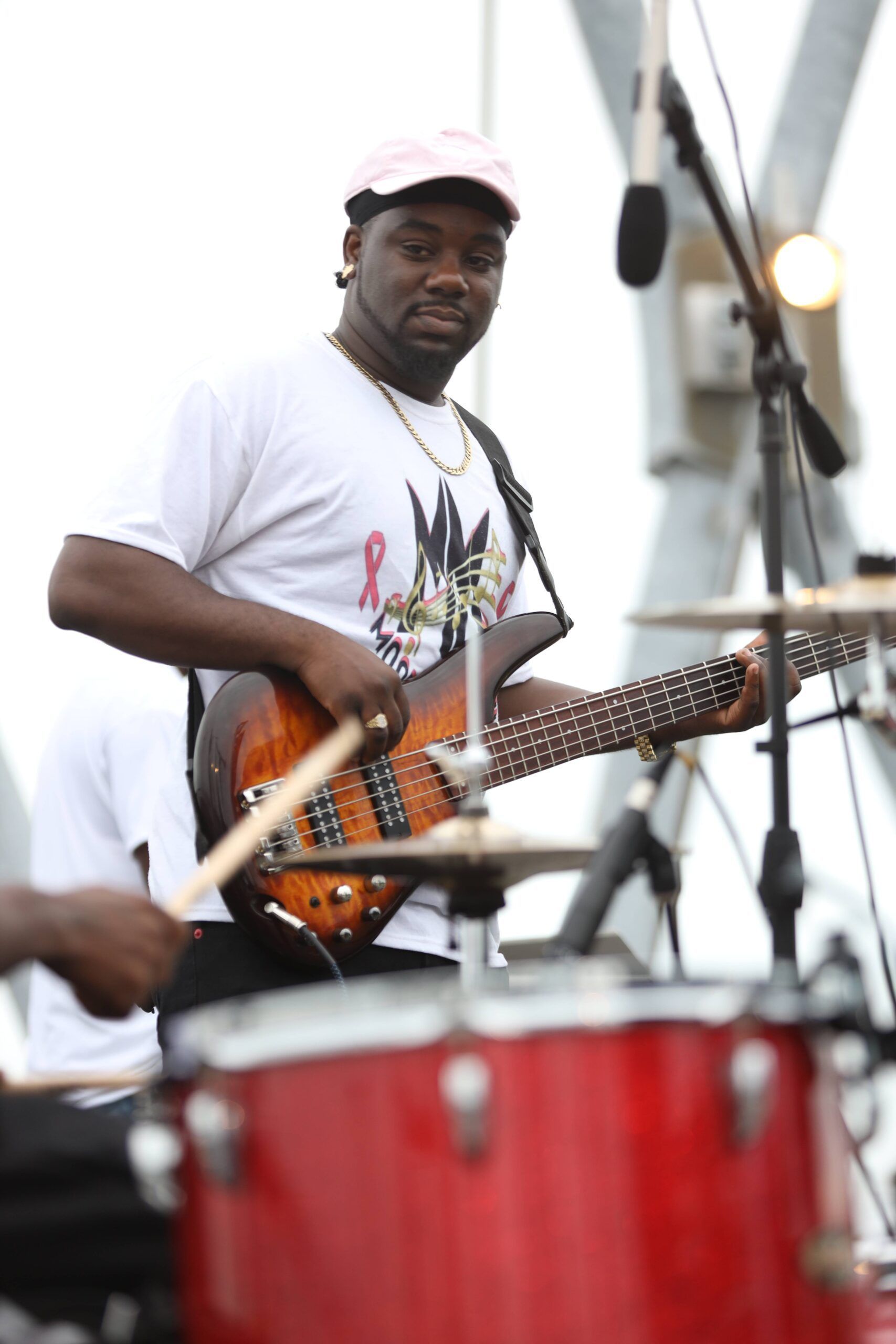 Musician playing electric bass behind red drums on an outdoor stage