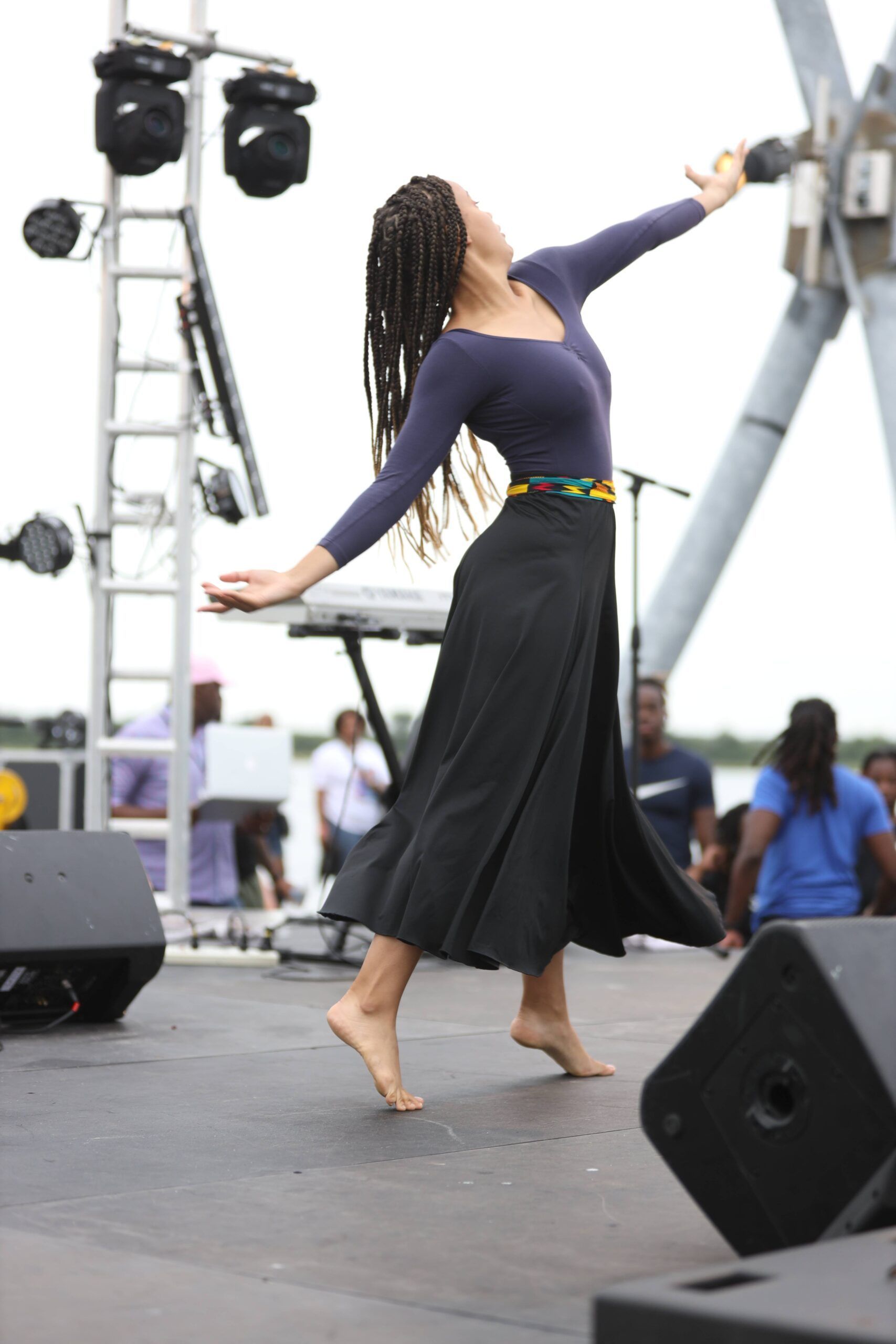 Dancer in navy top and black skirt performing on an outdoor stage with lighting rig and speakers
