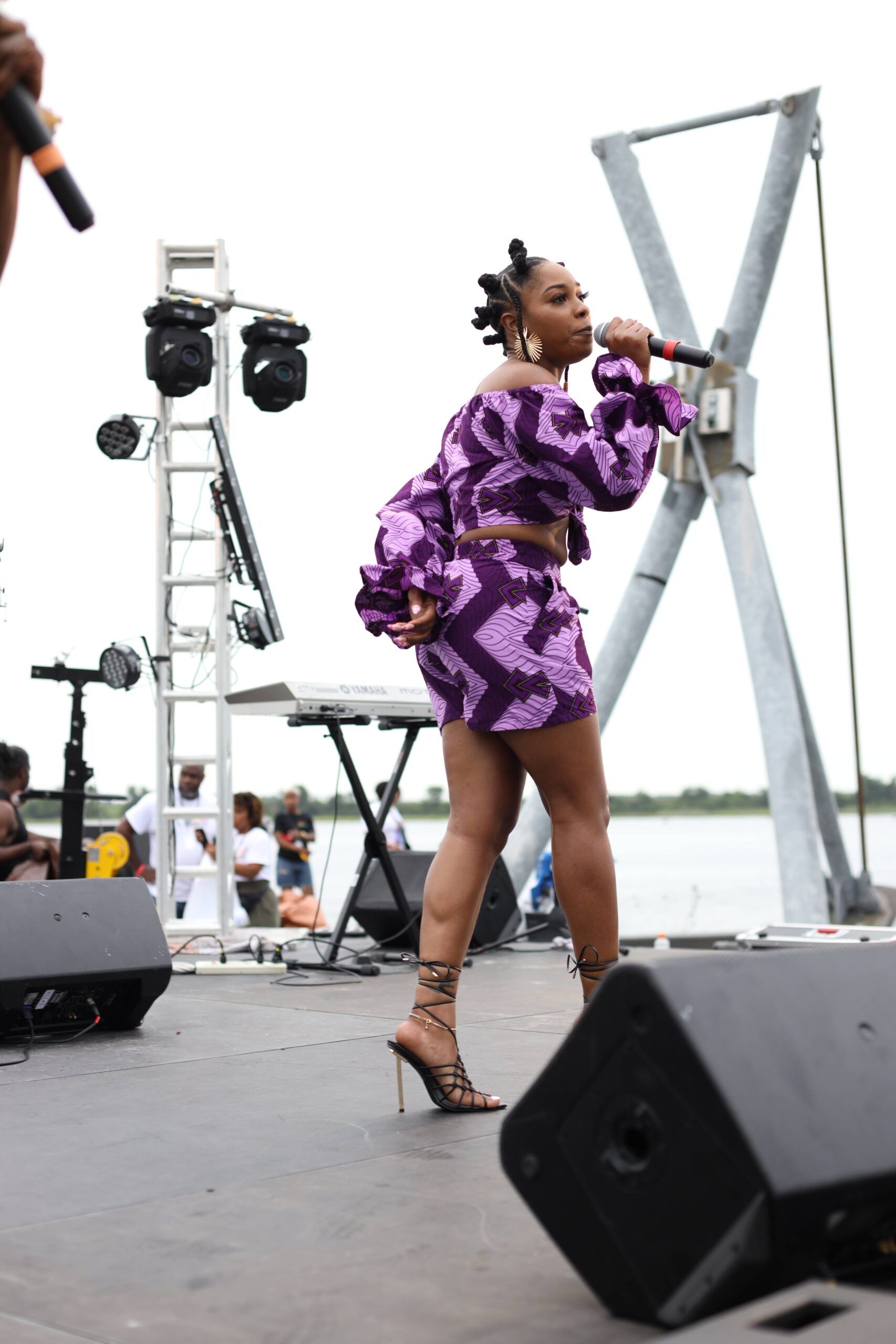 Performer in purple dress singing on an outdoor stage with microphone and speakers