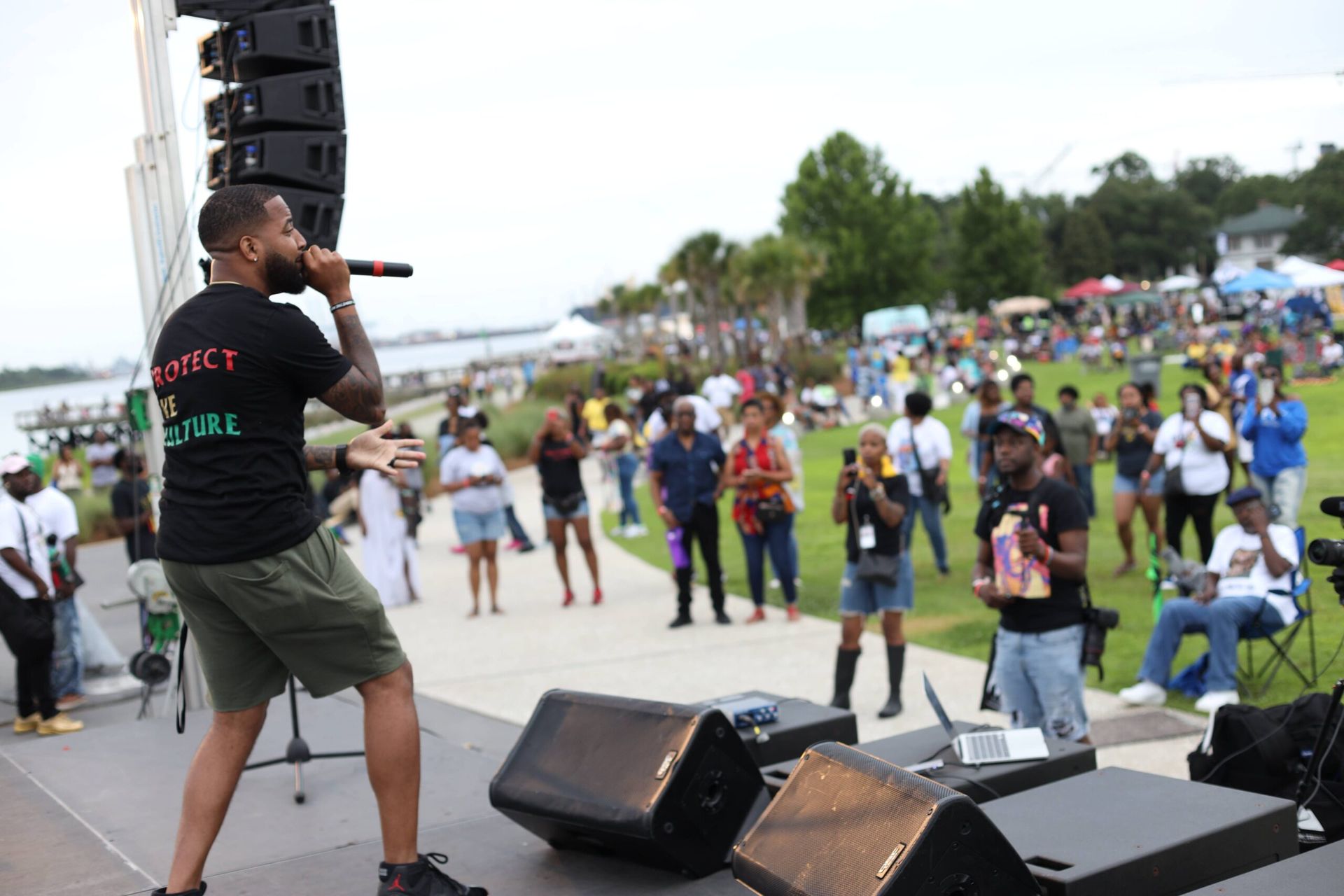 Performer speaking on outdoor stage to crowd at a park festival