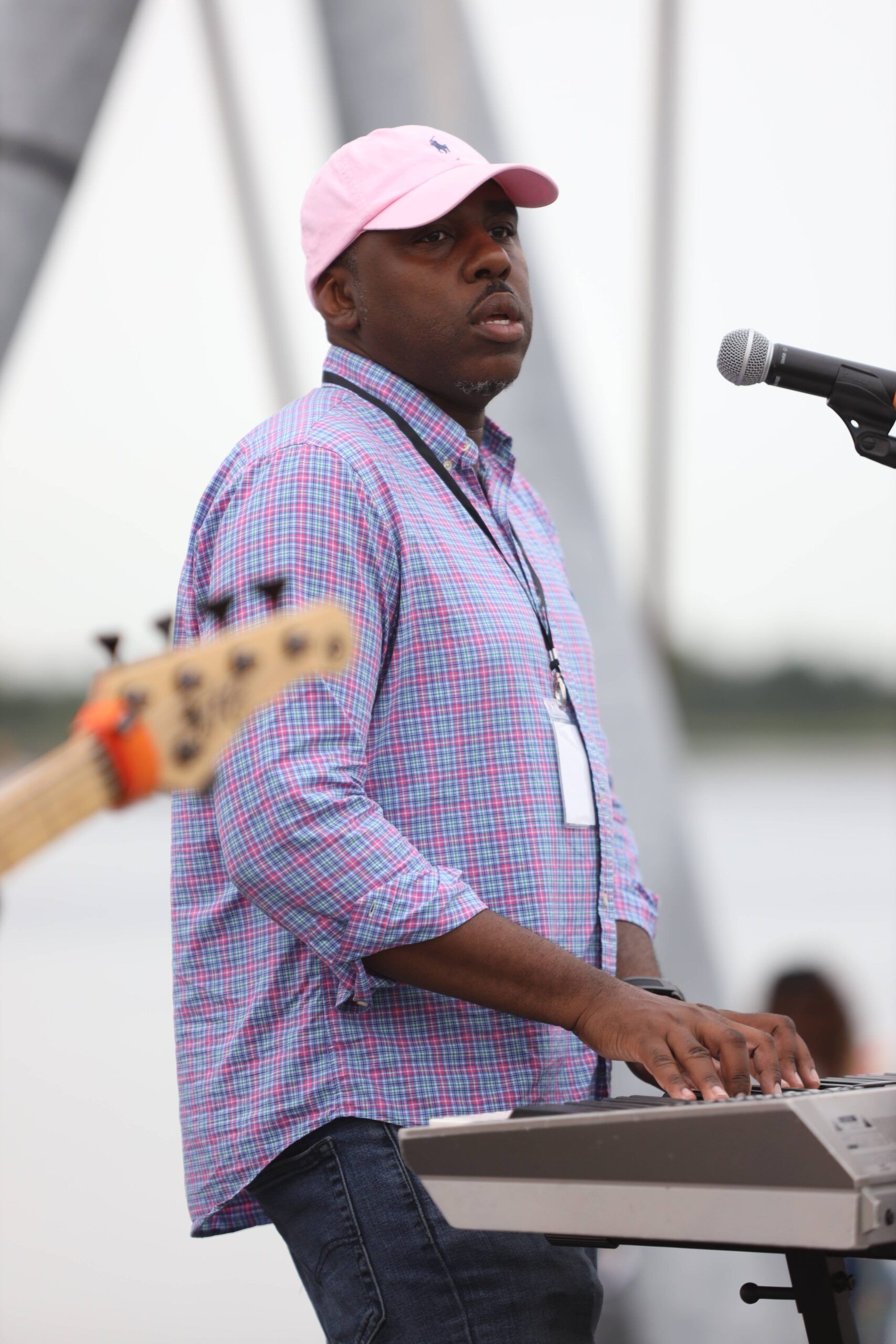Musician in pink cap playing keyboard on an outdoor stage beside a microphone