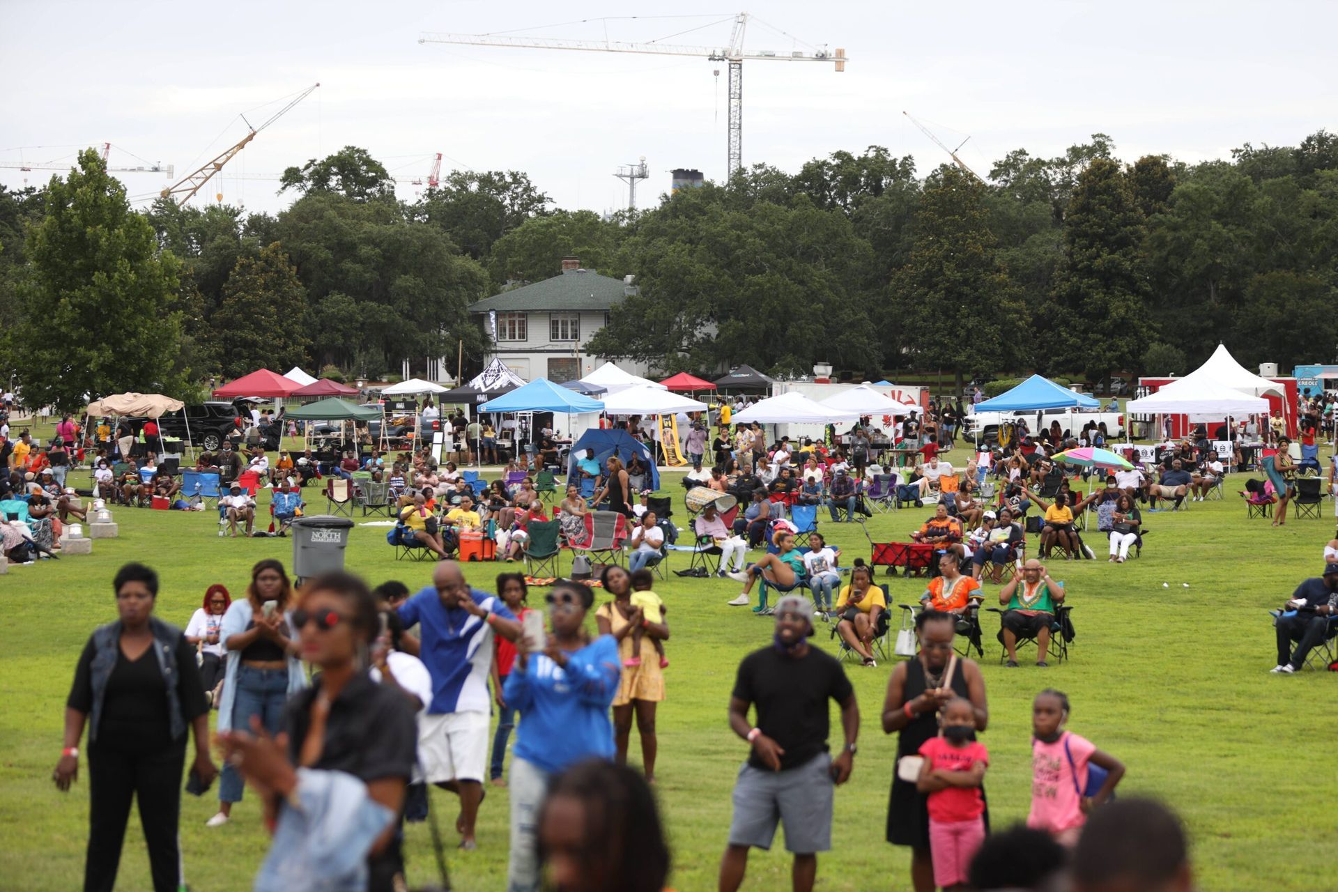 Crowded outdoor festival on a grassy field with tents, people sitting, and others walking in the foreground