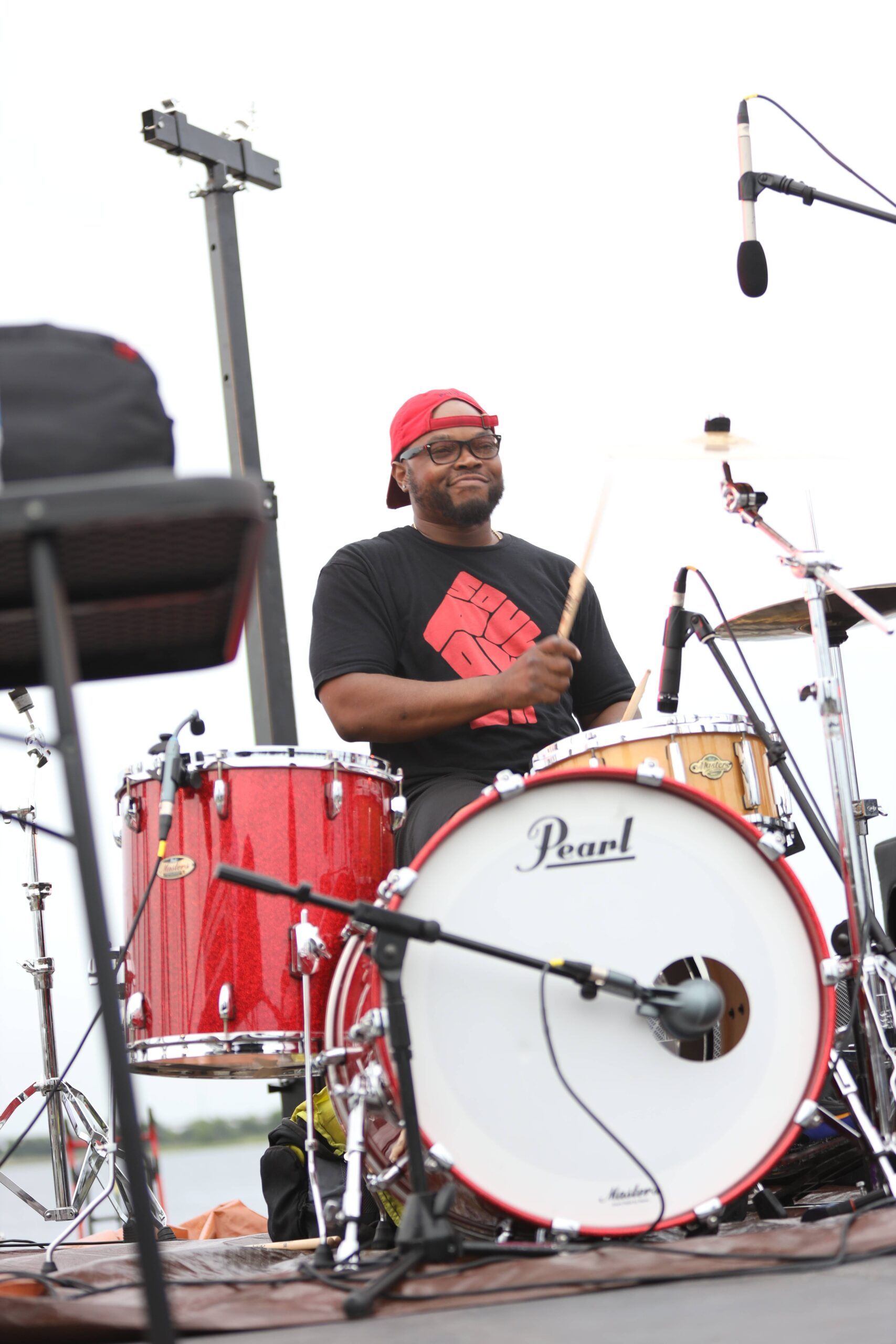 Drummer in red cap playing a red Pearl drum kit on an outdoor stage