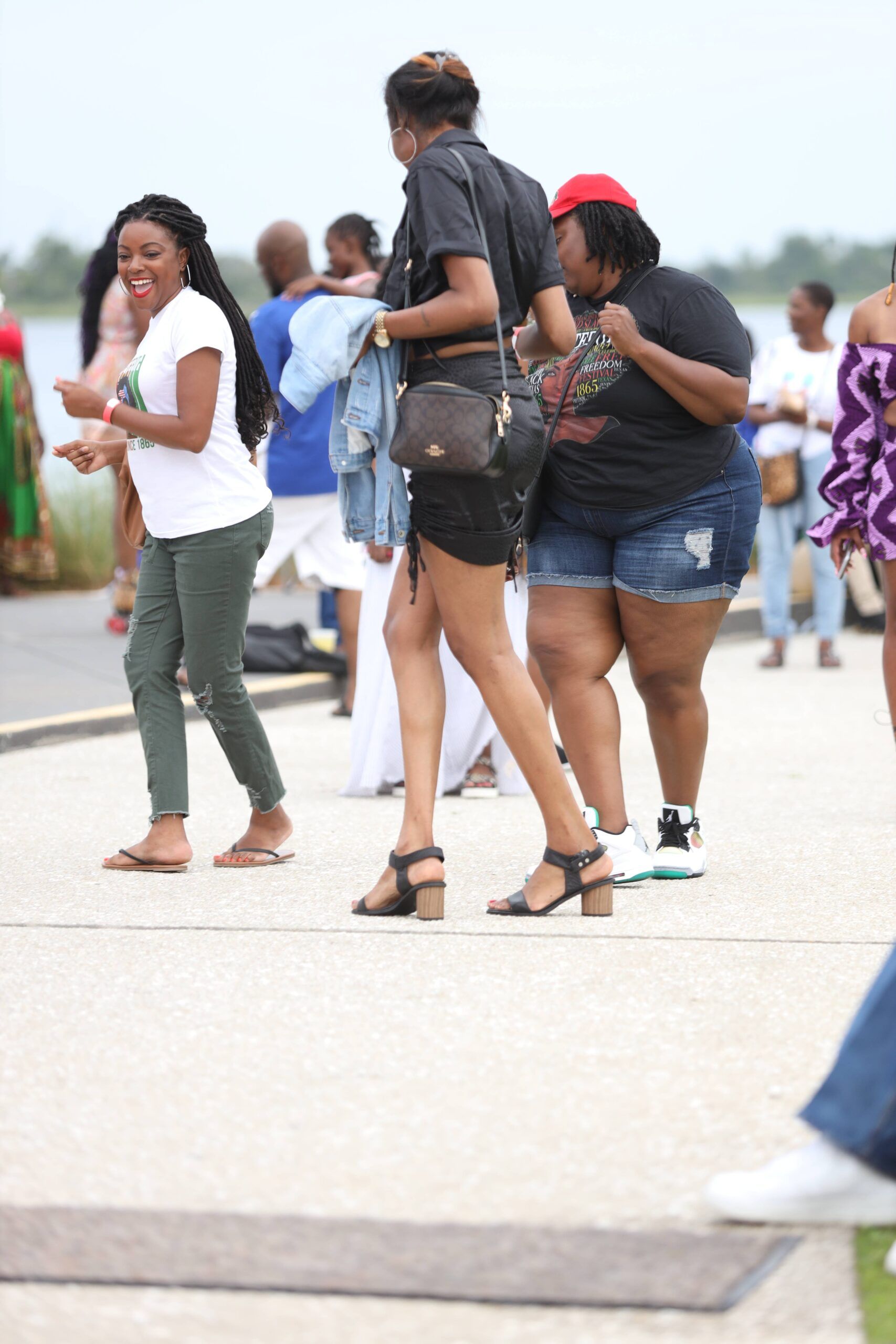 People walking outdoors on a paved road, with one person in black heels and denim shorts in the foreground