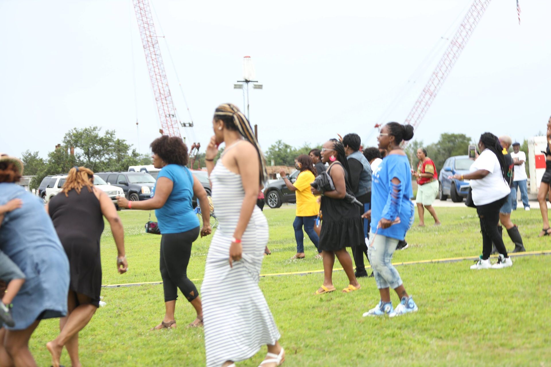 People dancing on a grassy field at an outdoor event with tall crane-like structures in the background