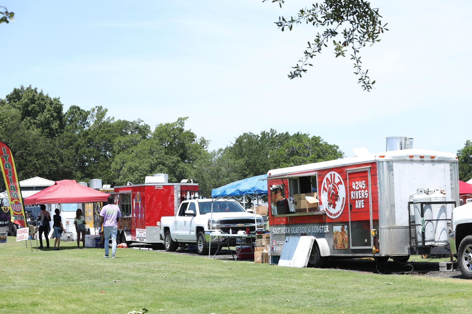 Food trucks and tents at an outdoor park event on a sunny day